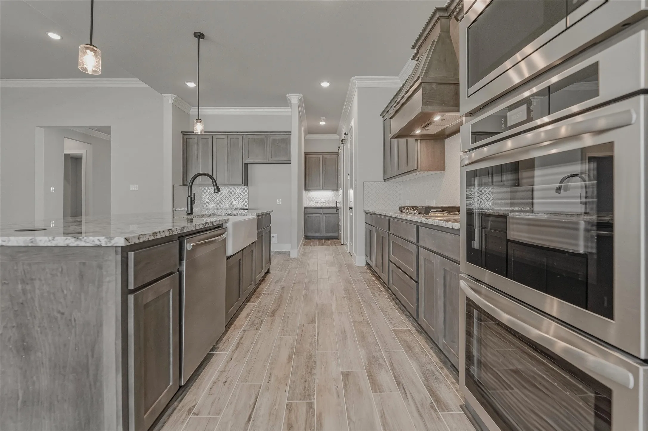 Modern kitchen featuring wood-finish flooring, light gray cabinetry, stainless steel appliances, a farmhouse sink, and granite countertops