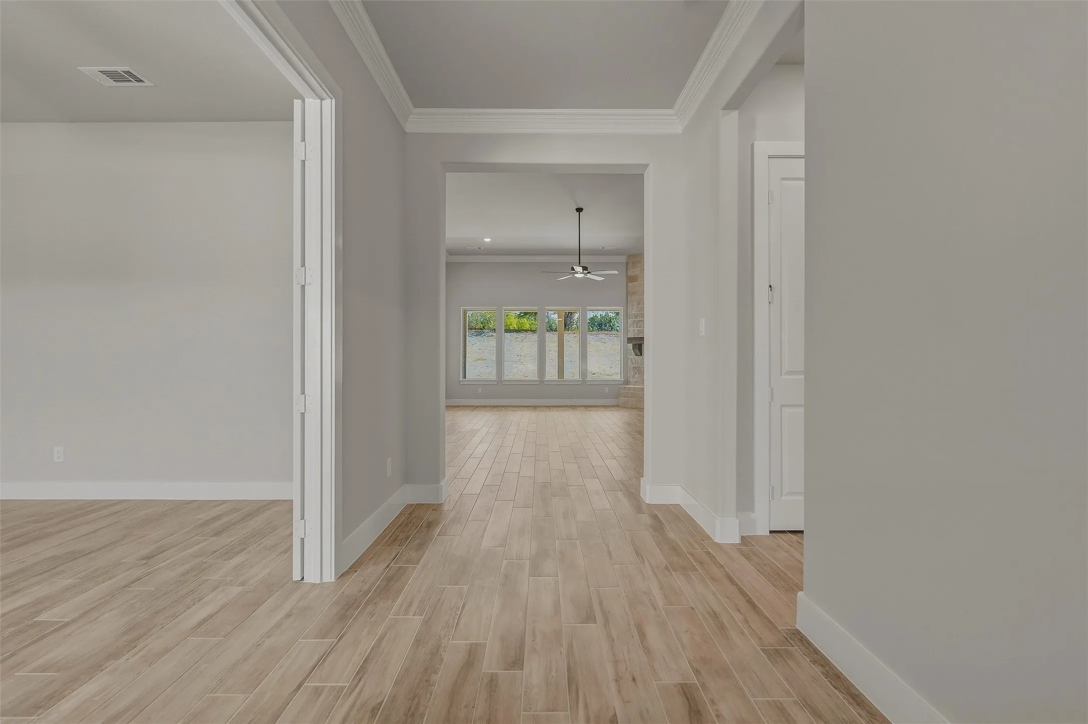 Hallway featuring wood-look tile flooring, light gray walls, white baseboards, and crown molding