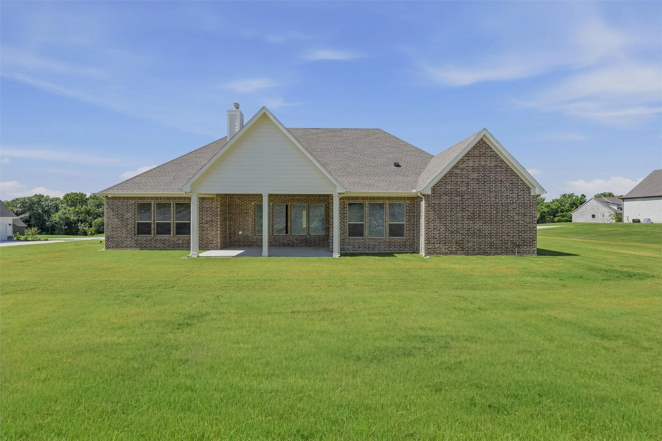 Expansive rear lawn featuring a brick exterior, covered patio, multiple windows, and a prominent chimney