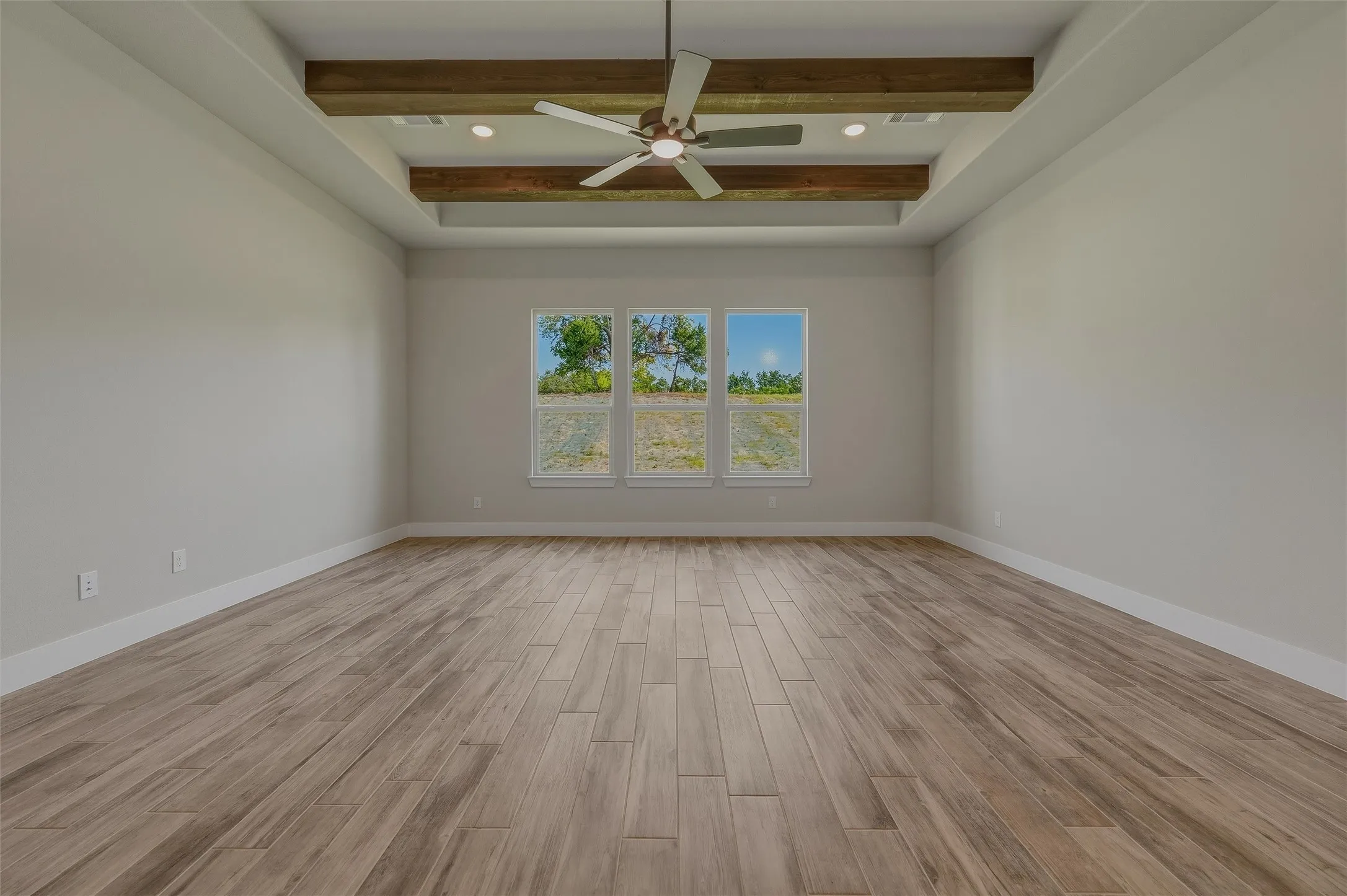 Spacious room featuring wood-finish flooring, a tray ceiling with exposed wood beams, and recessed lighting