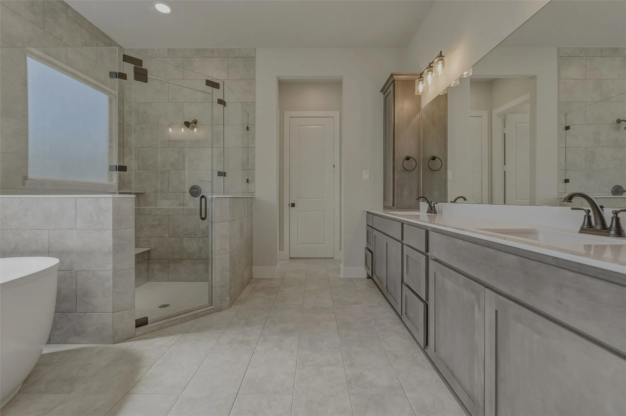 Spacious bathroom featuring a frameless glass shower enclosure with a built-in bench, a freestanding soaking tub, dual vanity with undermount sinks and dark bronze fixtures, a full-width mirror, and a tall built-in storage cabinet