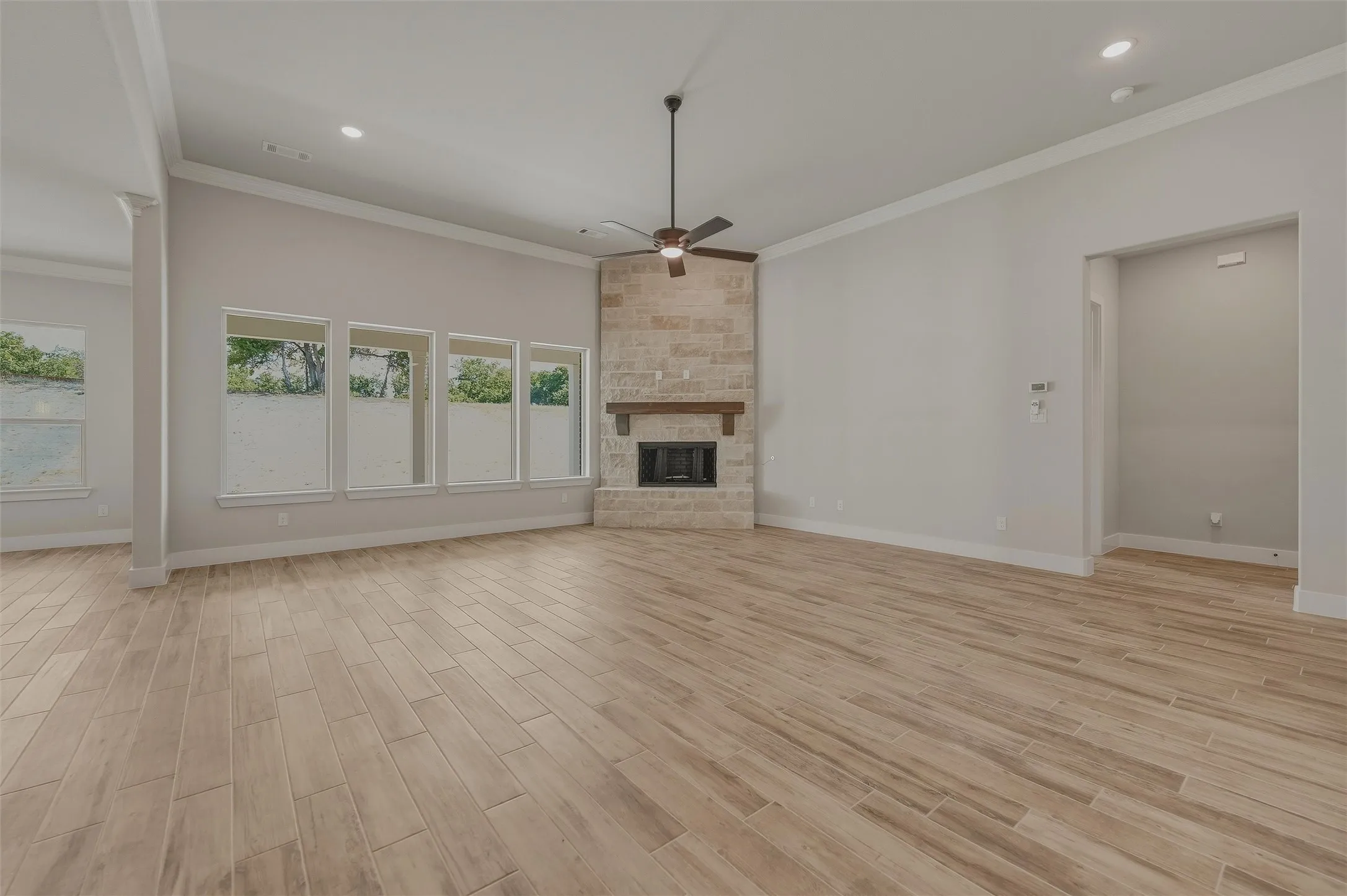 Spacious living area featuring wood-finish flooring, a corner stone fireplace with a wood mantle, a ceiling fan, recessed lighting, and multiple windows