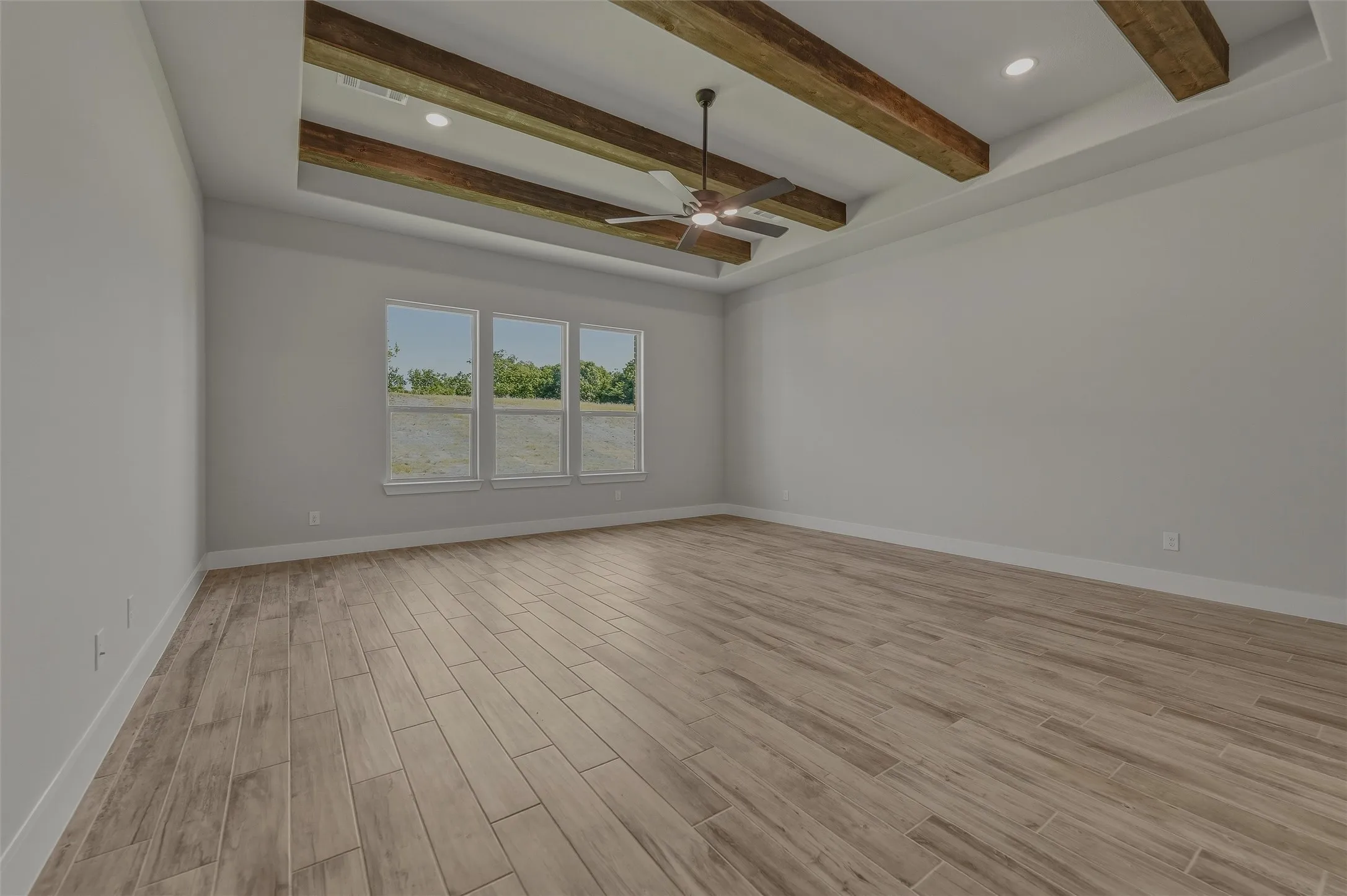 Spacious room featuring a tray ceiling with exposed wood beams, a modern ceiling fan, recessed lighting, and three large windows