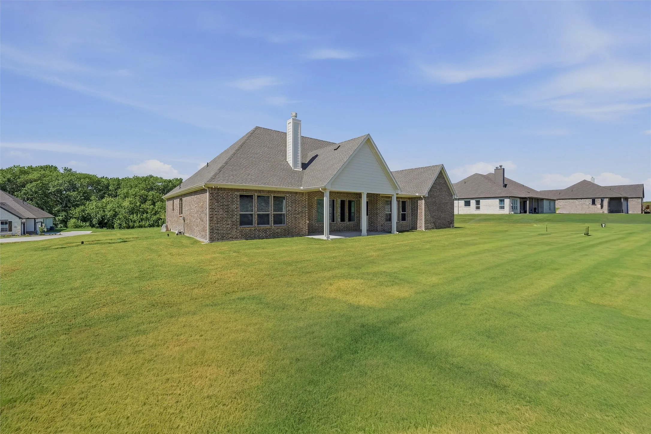 Brick exterior home featuring a covered patio, multiple rear windows, a gabled roofline, and a chimney stack
