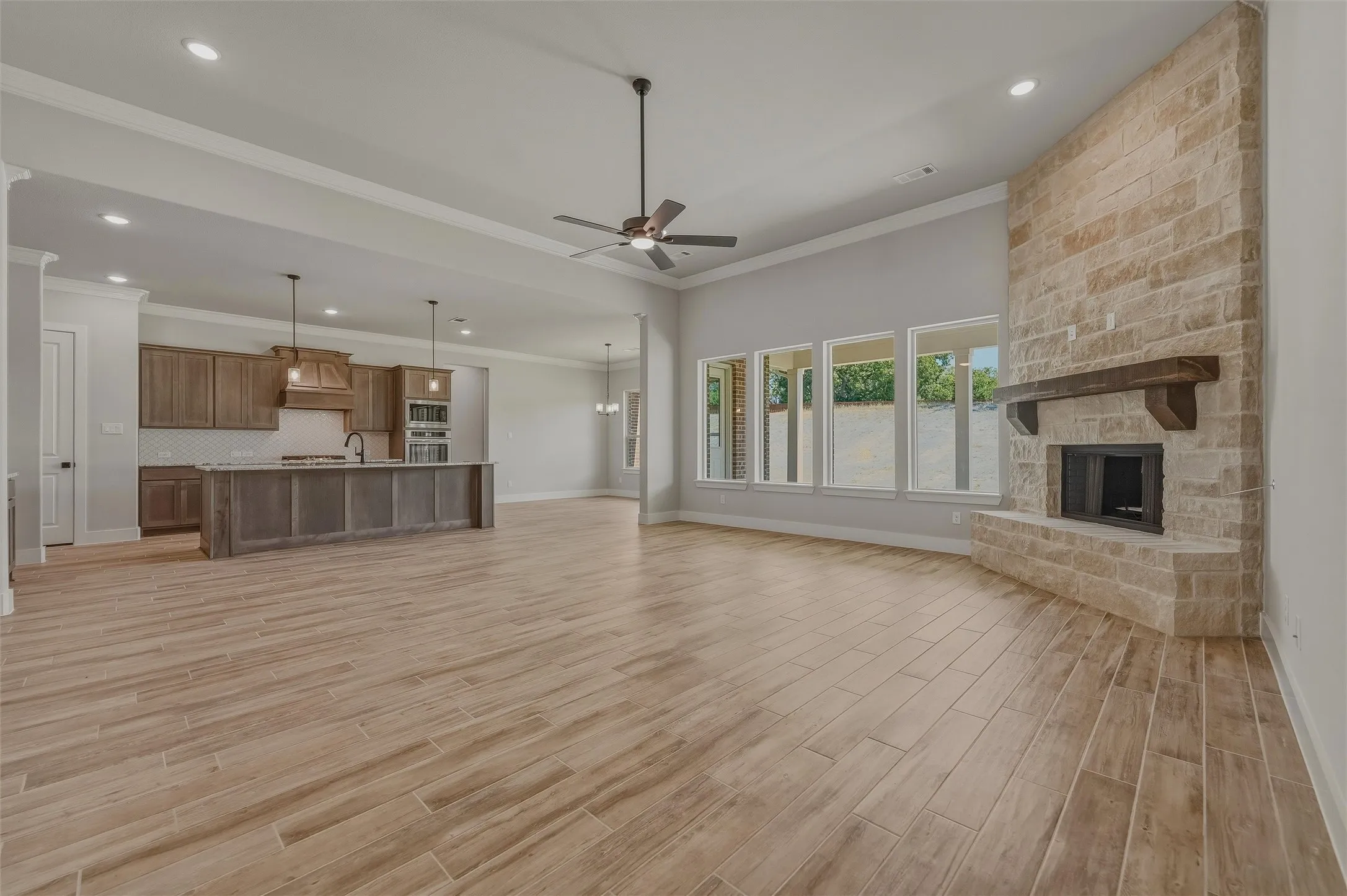 Spacious living area featuring a floor-to-ceiling stone fireplace with a wood mantel, wood-finish flooring, and multiple windows
