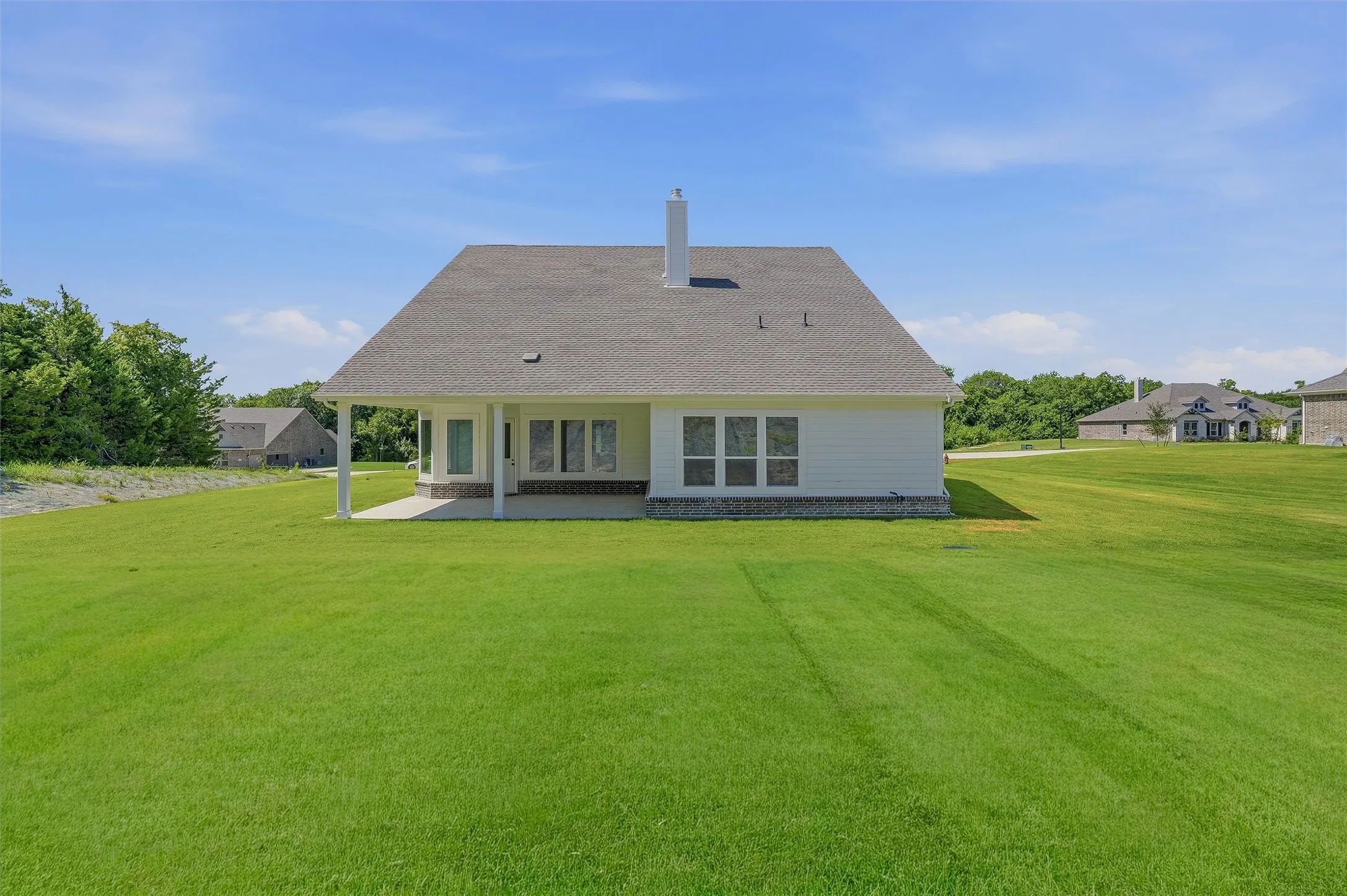 Expansive green lawn surrounds the white siding exterior of this residence, featuring a covered patio and multiple windows