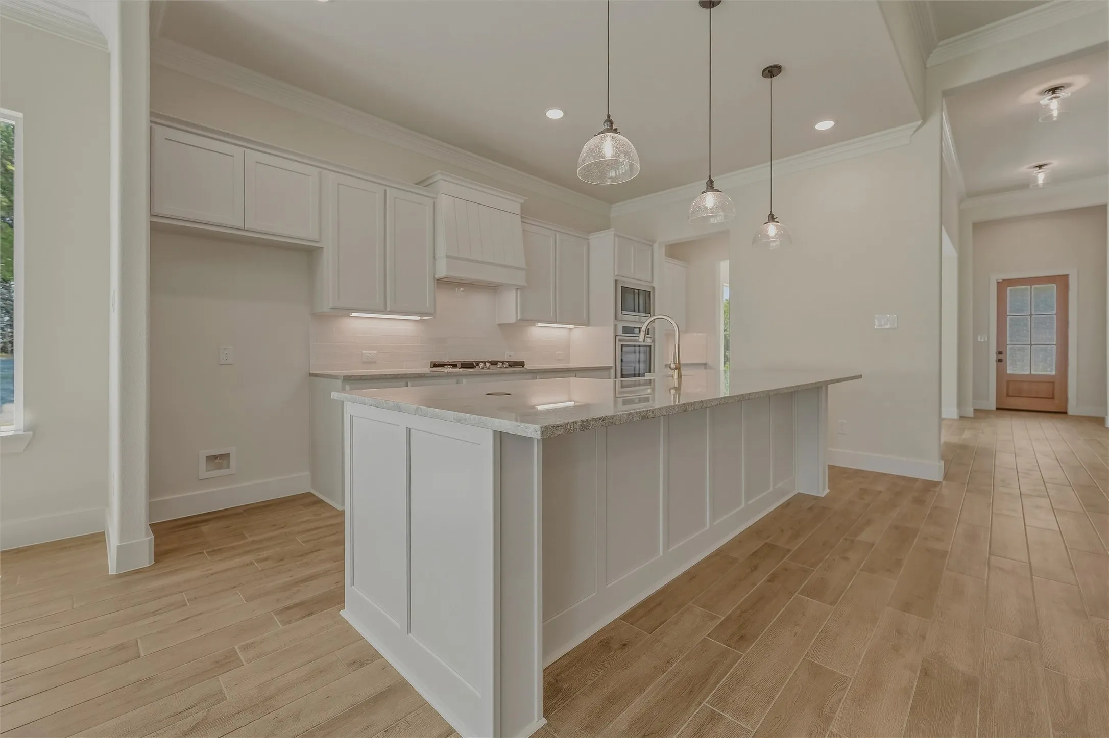 Kitchen featuring an expansive island with a light-toned countertop, white shaker-style cabinetry, and wood-finish flooring