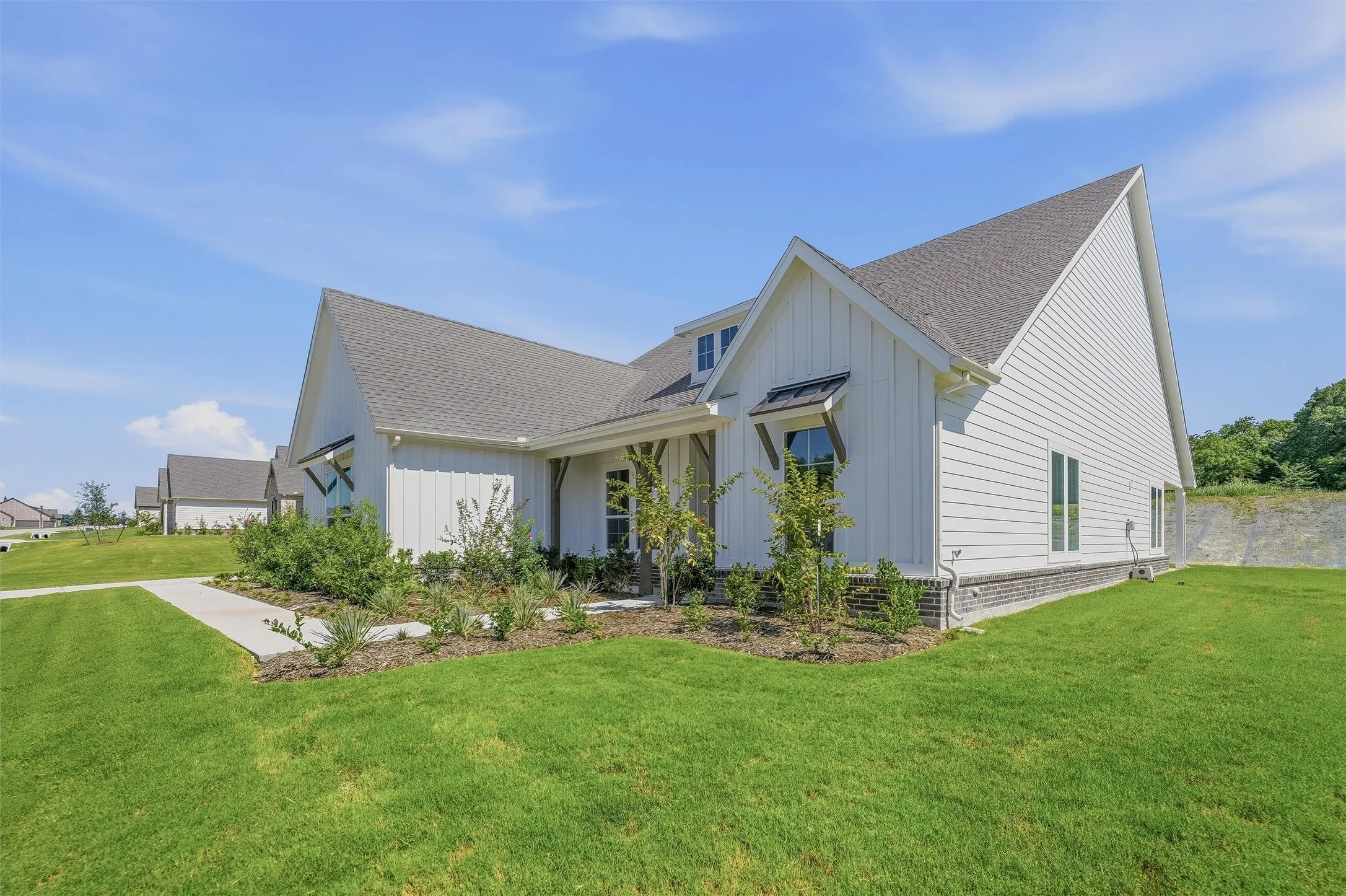 Contemporary farmhouse exterior featuring white board-and-batten siding, horizontal siding, a dark shingle roof, and dark brick wainscoting