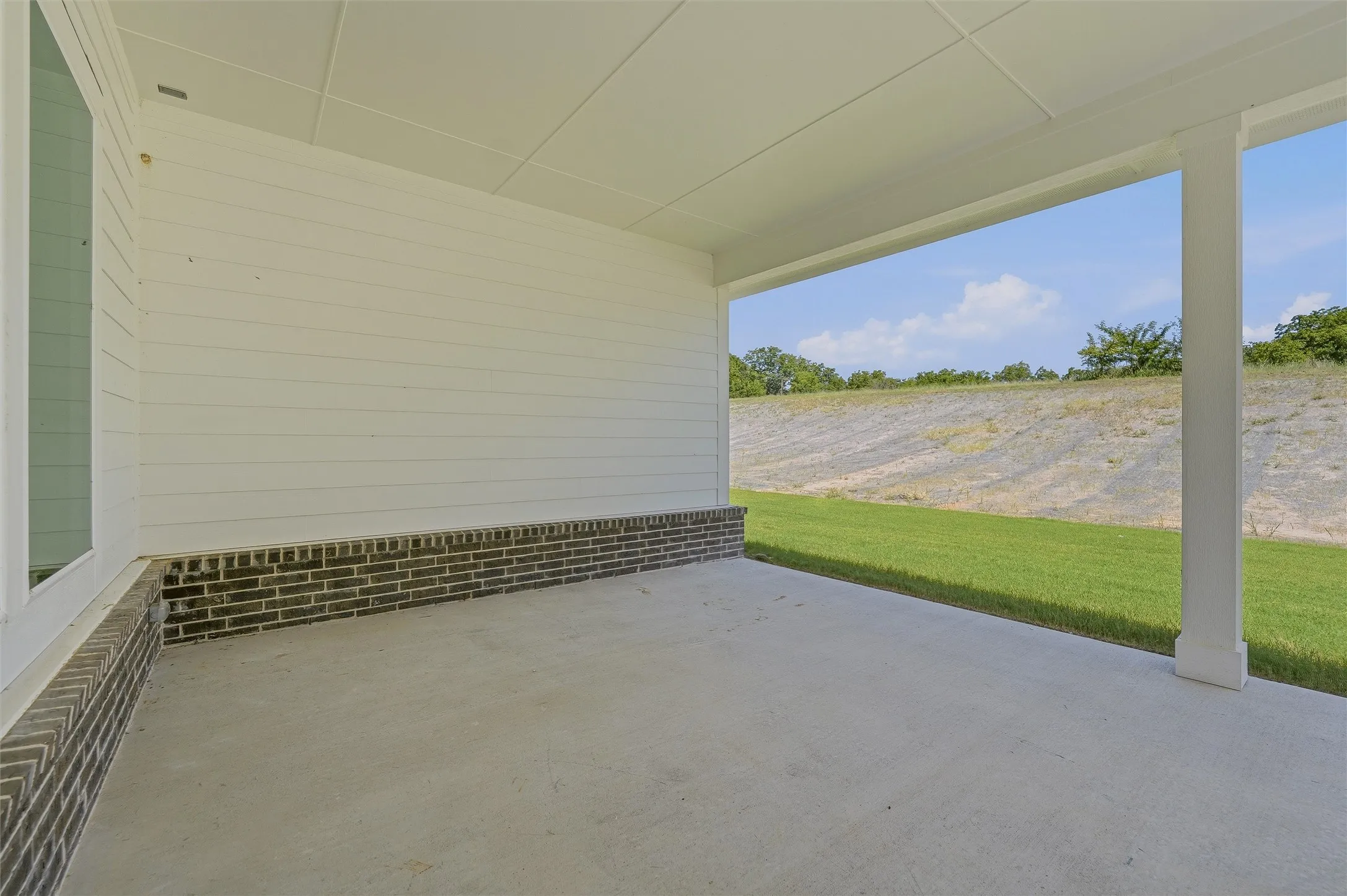 Covered outdoor patio with a concrete surface, white siding, and a dark brick foundation