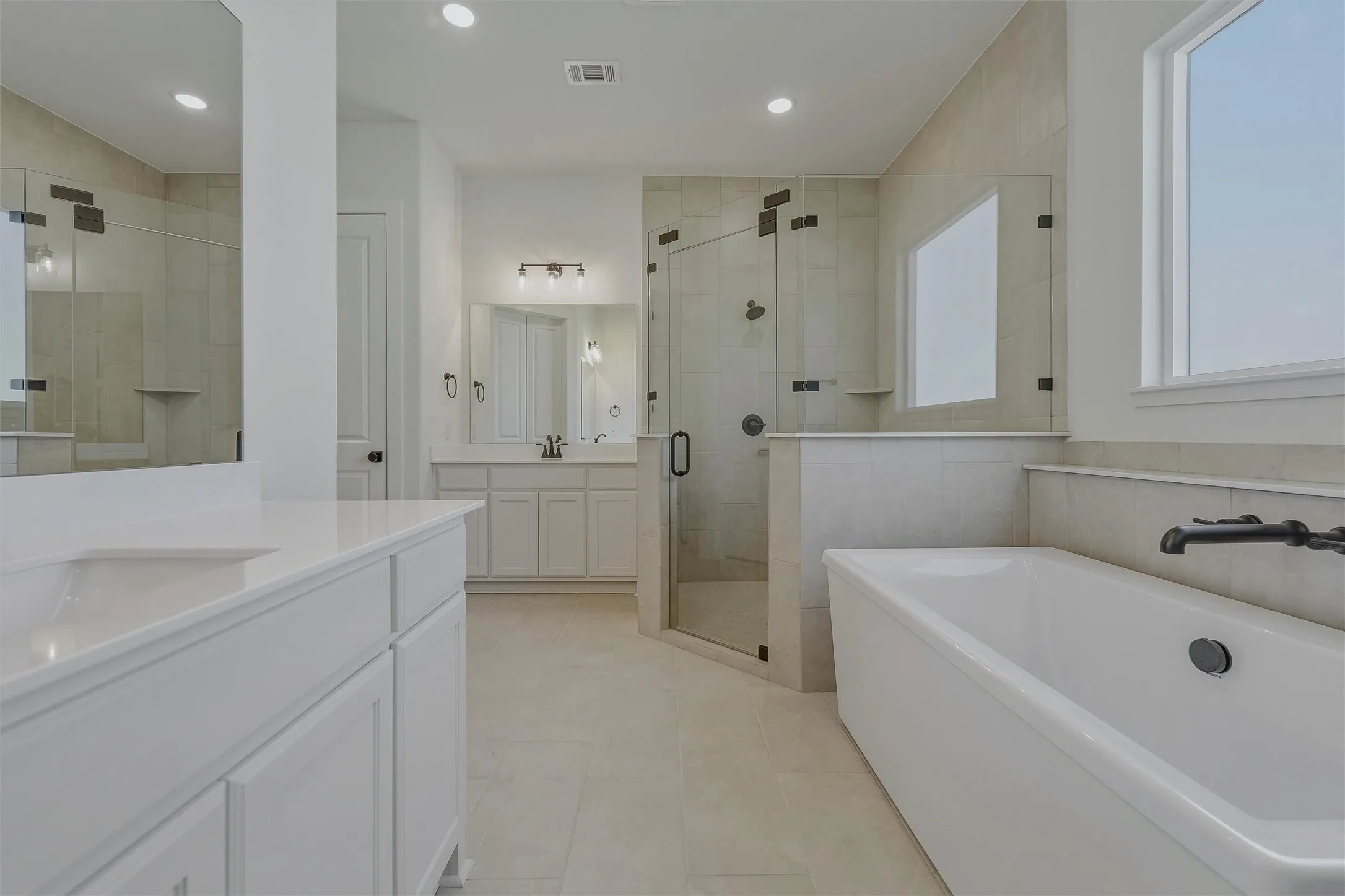 Contemporary bathroom featuring a freestanding tub, glass-enclosed shower, dual vanities with white cabinetry, quartz countertops, and recessed lighting