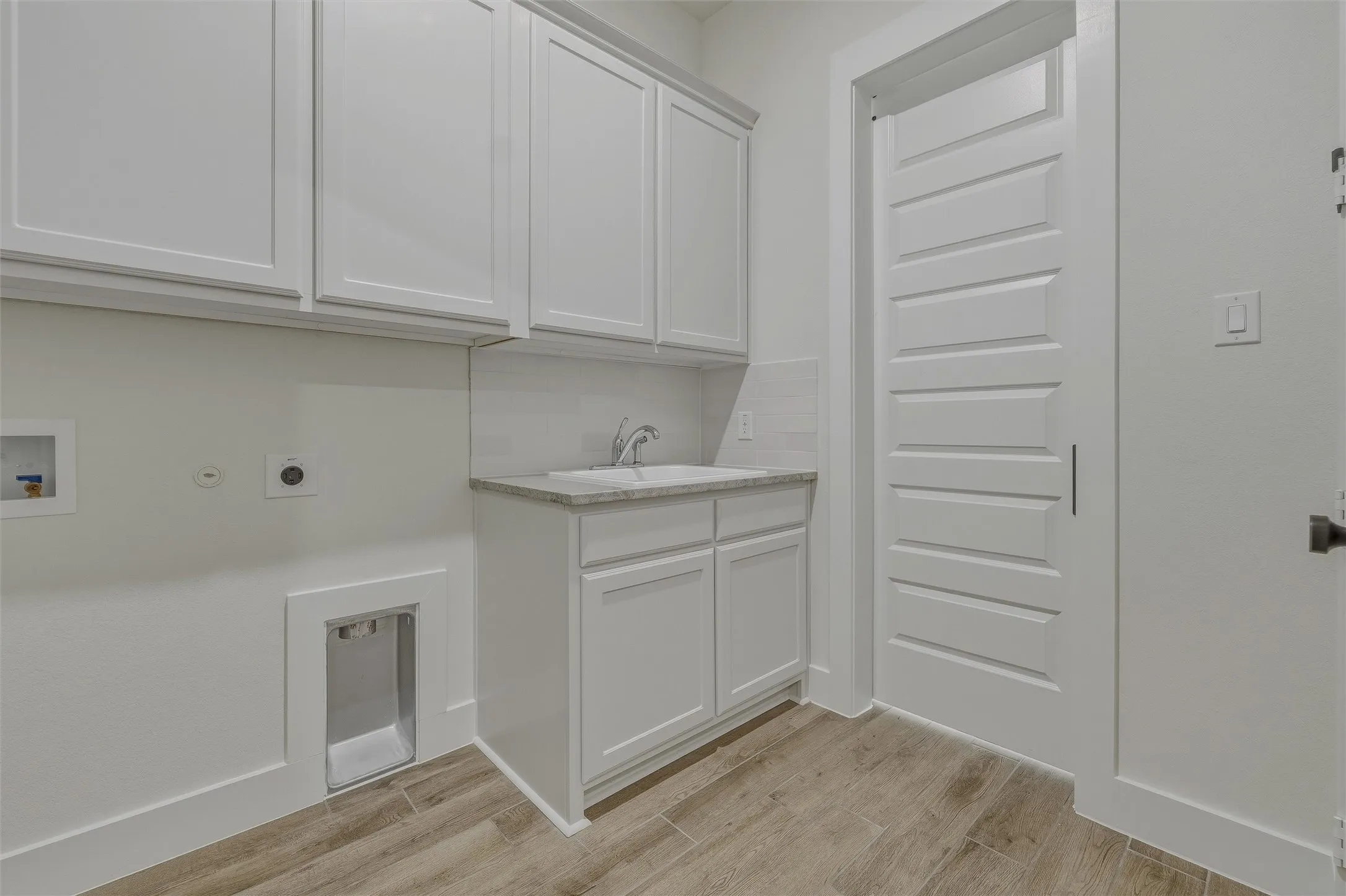 Laundry area featuring abundant white cabinetry, a utility sink with a stone-finish countertop, and wood-look tile flooring
