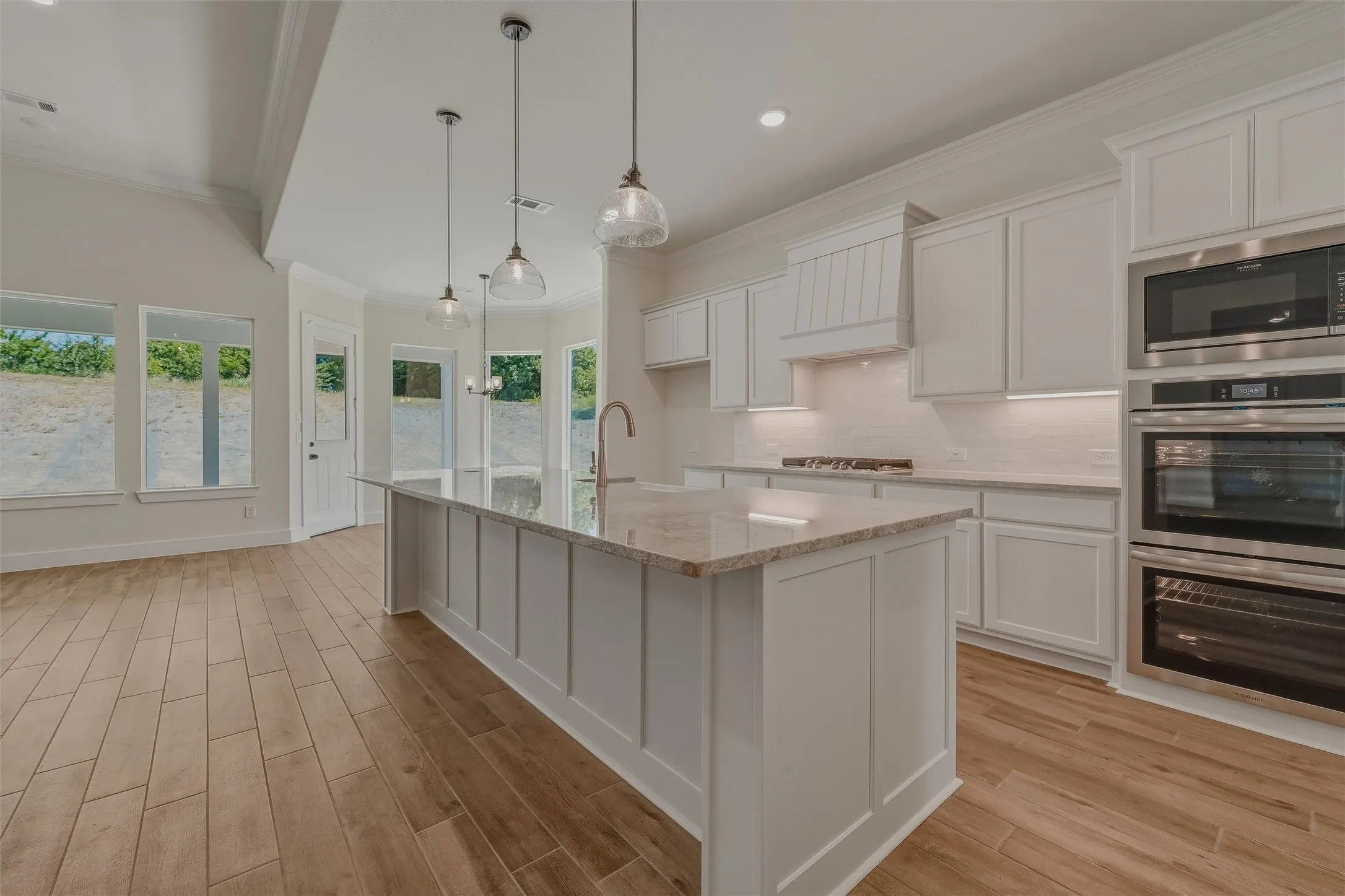 Contemporary kitchen featuring a large island with a light-toned countertop, white cabinetry, integrated stainless steel appliances, and wood-finish flooring