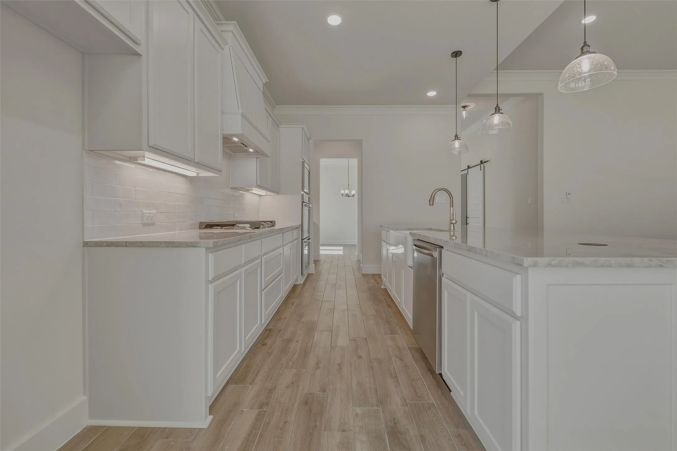 Spacious kitchen with wood-finish flooring, white shaker-style cabinetry, light-toned countertops, and a subway tile backsplash