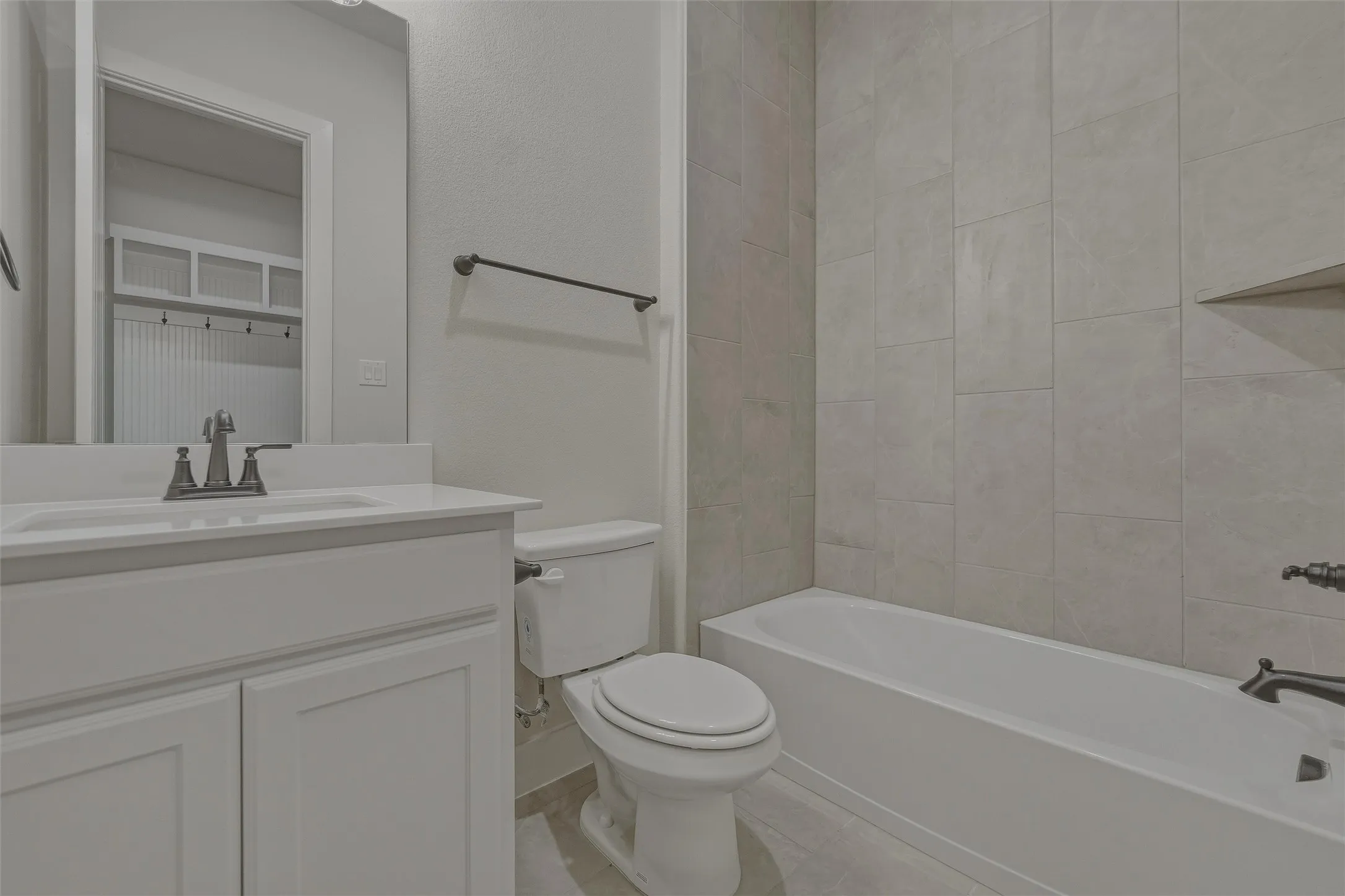 Bathroom featuring a white vanity with integrated sink, brushed nickel faucet, full-width mirror, and subway tile shower surround with a built-in shelf