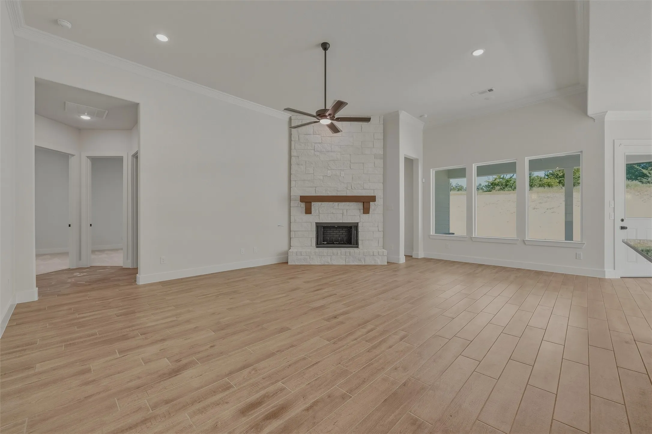 Spacious living area featuring wood-finish flooring, a stone fireplace with a wood mantel, multiple large windows, a ceiling fan, and recessed lighting