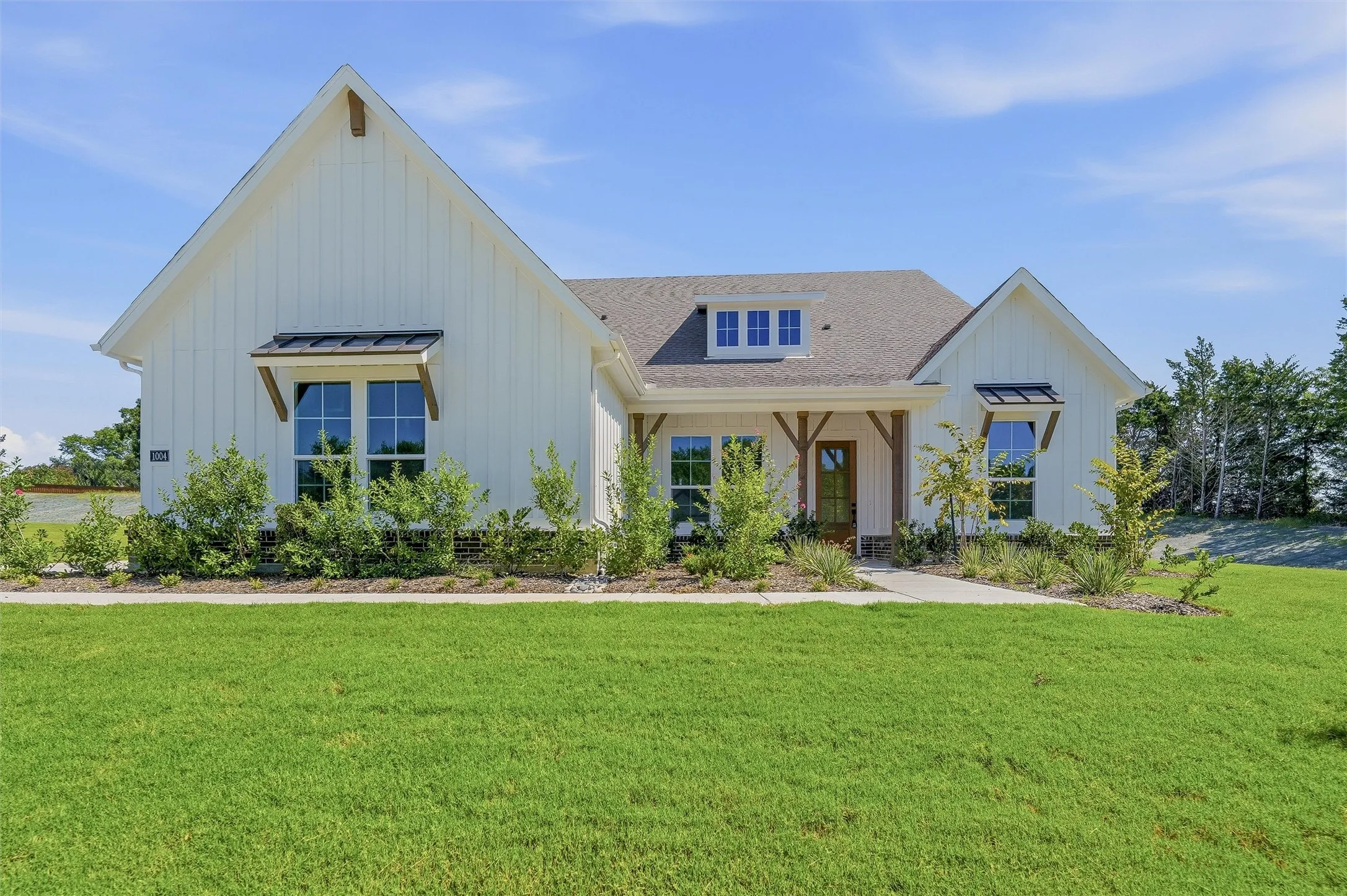 Modern farmhouse exterior featuring white board and batten siding, a gray shingle roof, and dark window awnings