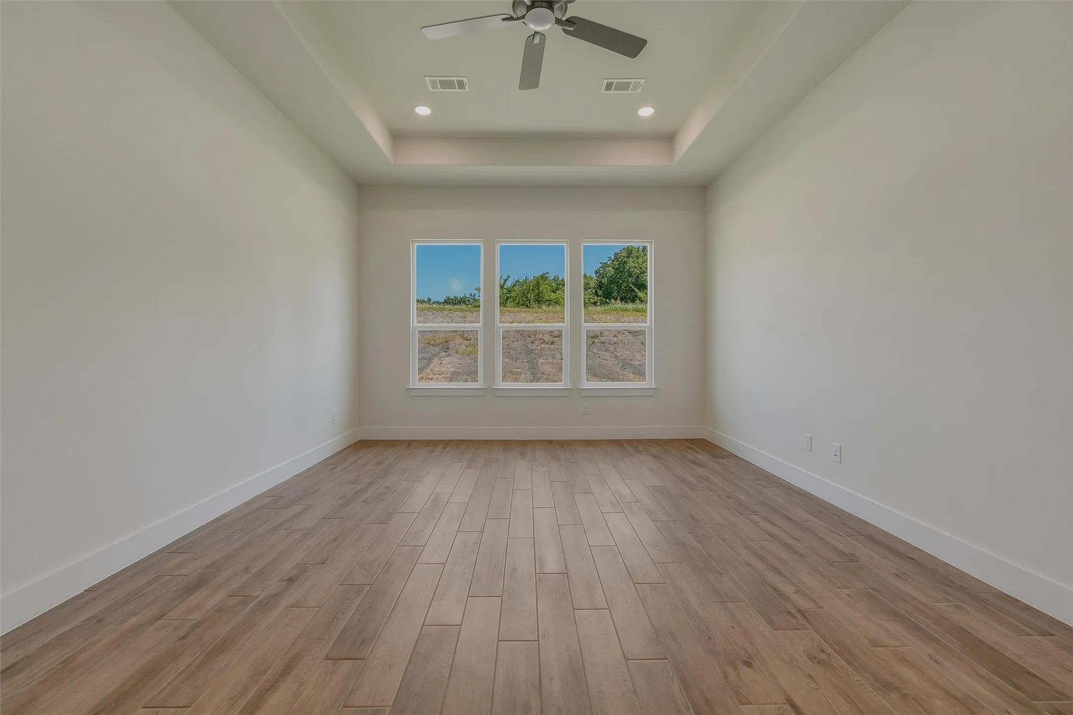 Spacious room featuring wood-finish flooring, a tray ceiling, recessed lighting, and a ceiling fan