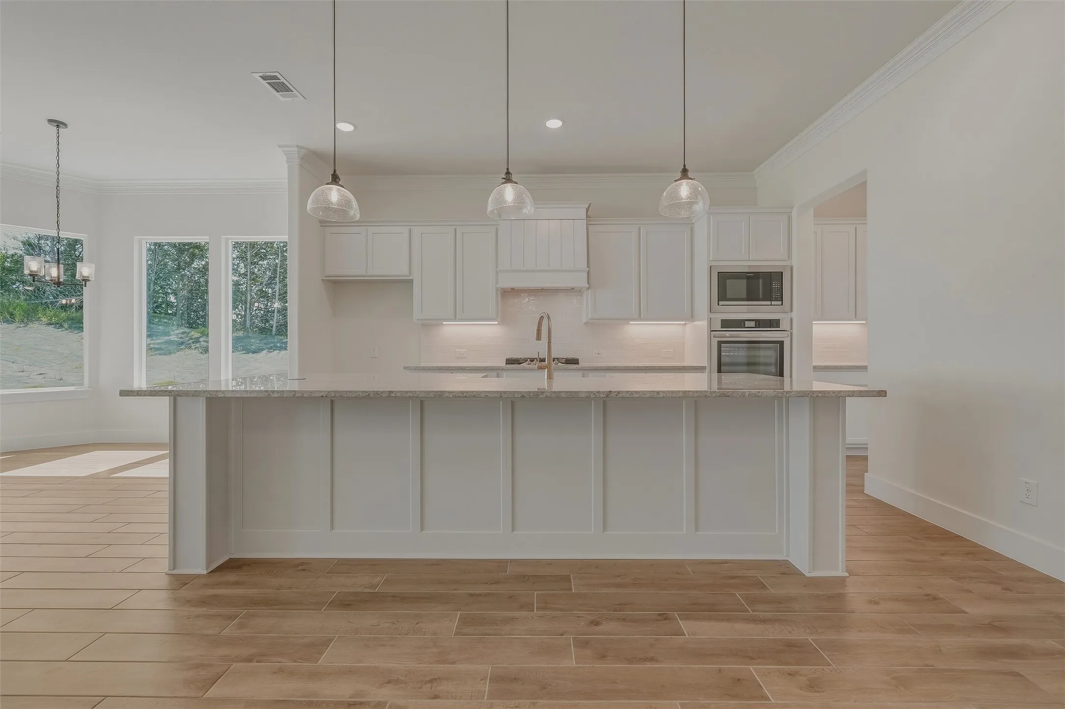 Spacious kitchen featuring a central island with integrated sink, white cabinetry, integrated double ovens, and wood-finish flooring