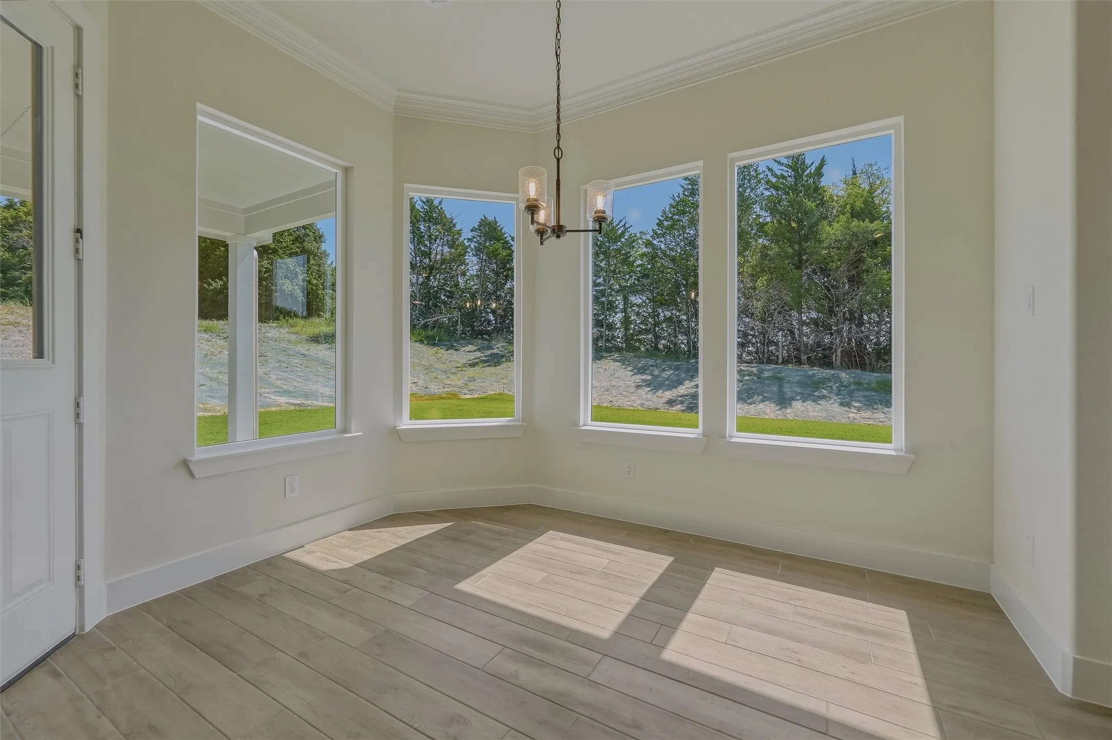 Light-filled room featuring wood-finish flooring, crisp white trim, crown molding, and a modern three-light chandelier
