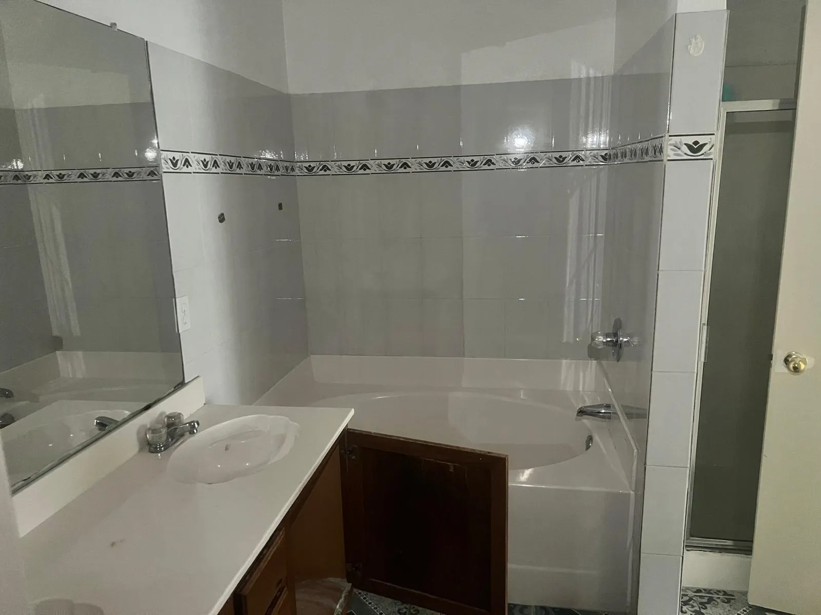 Bathroom featuring a built-in tub, tiled shower surround with decorative accent, a vanity with an integrated sink, polished chrome faucet, and a large wall-mounted mirror