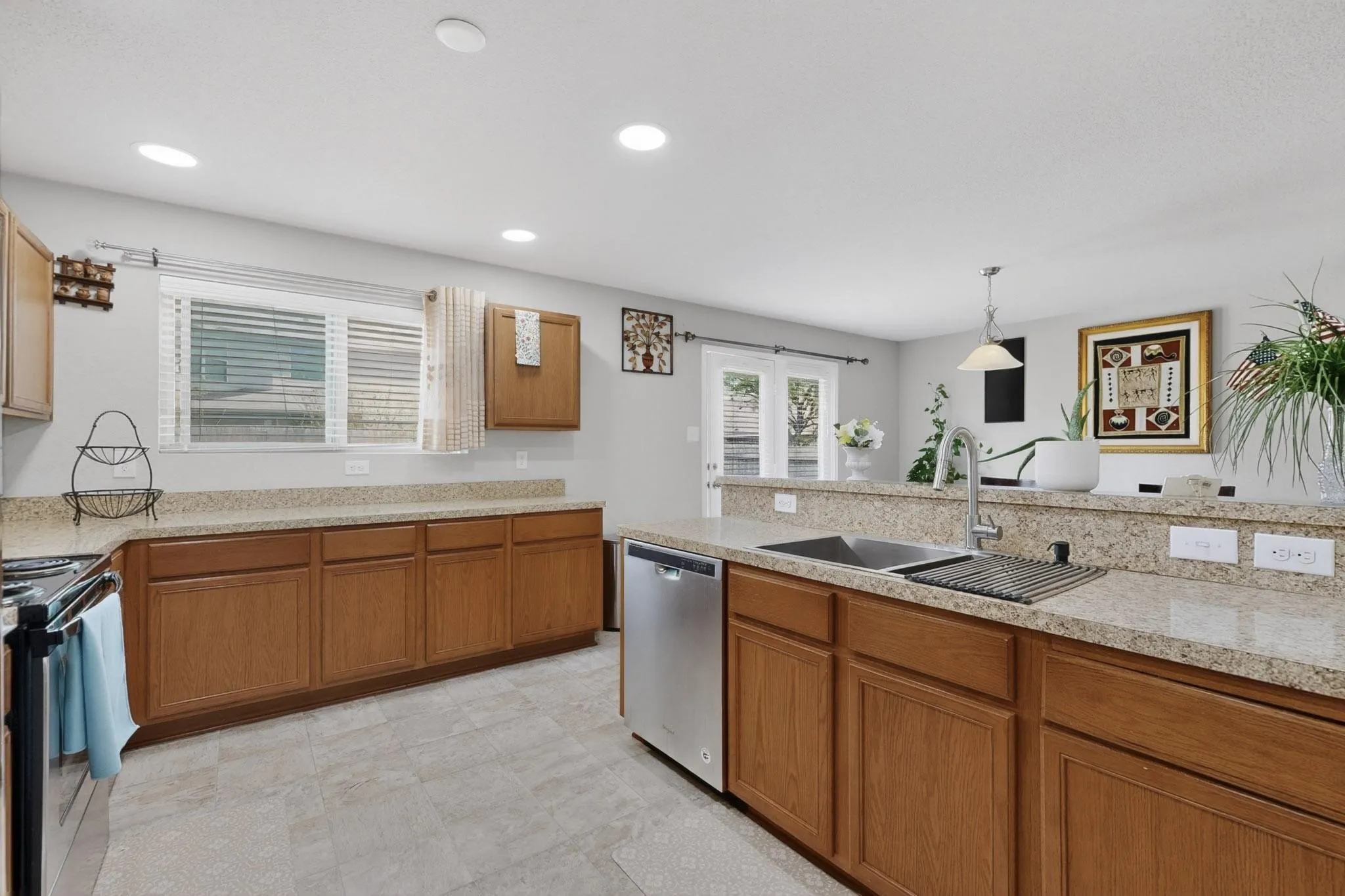 Kitchen featuring wood finish cabinetry, light stone countertops, stainless steel appliances, and pendant lighting