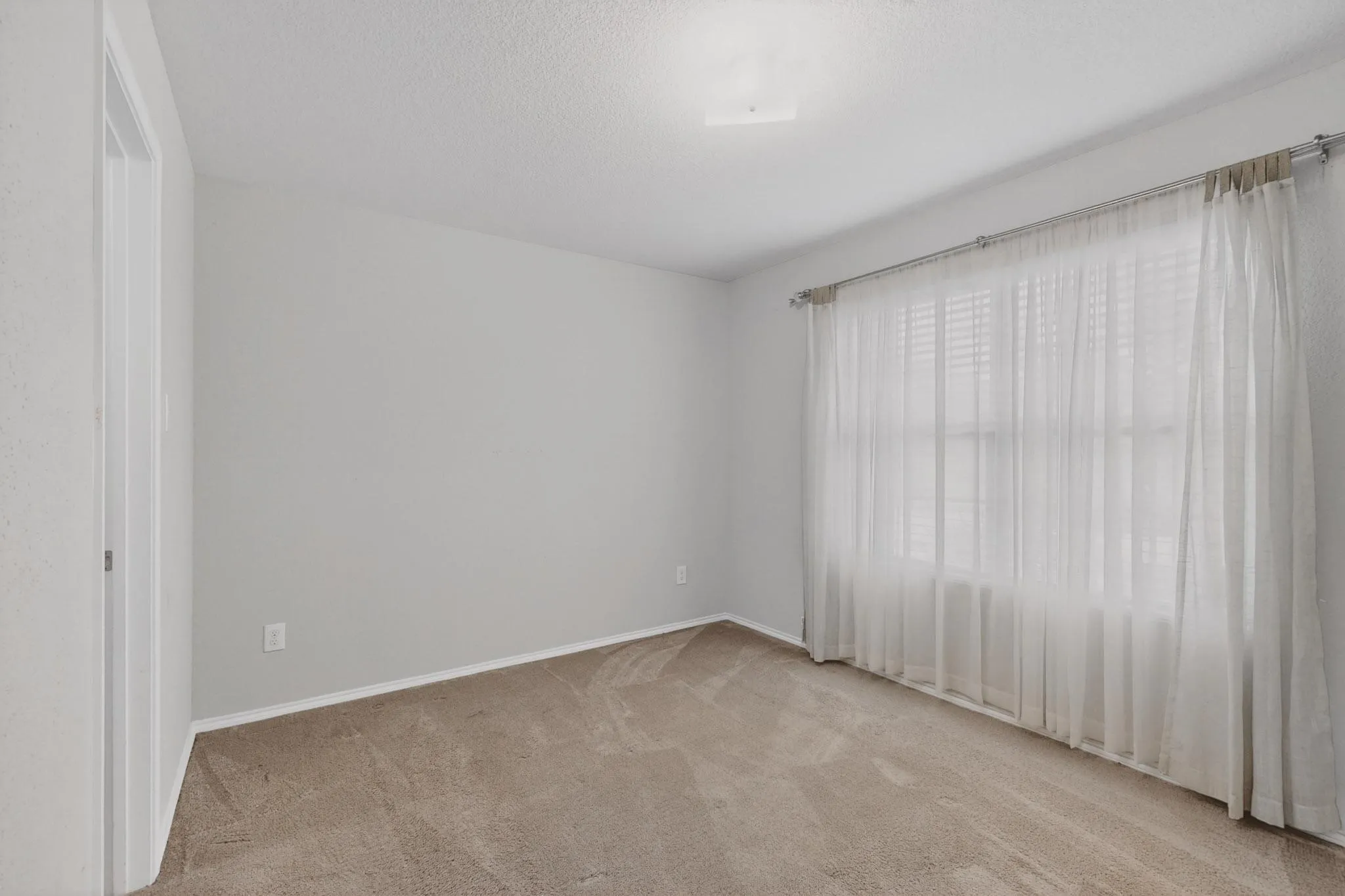Empty room with light colored carpet and a textured ceiling
