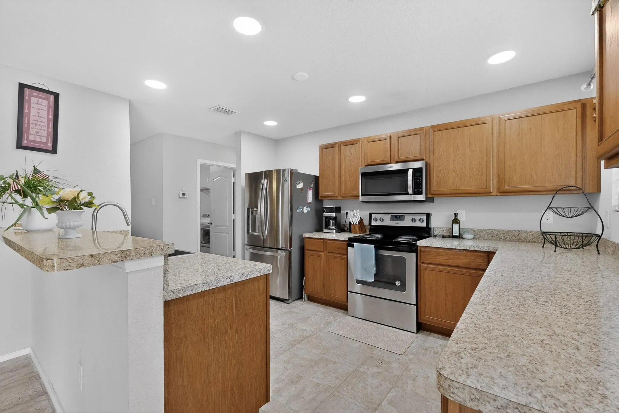 Kitchen featuring stainless steel appliances, light countertops, wood finish cabinets, recessed lighting, and a breakfast bar