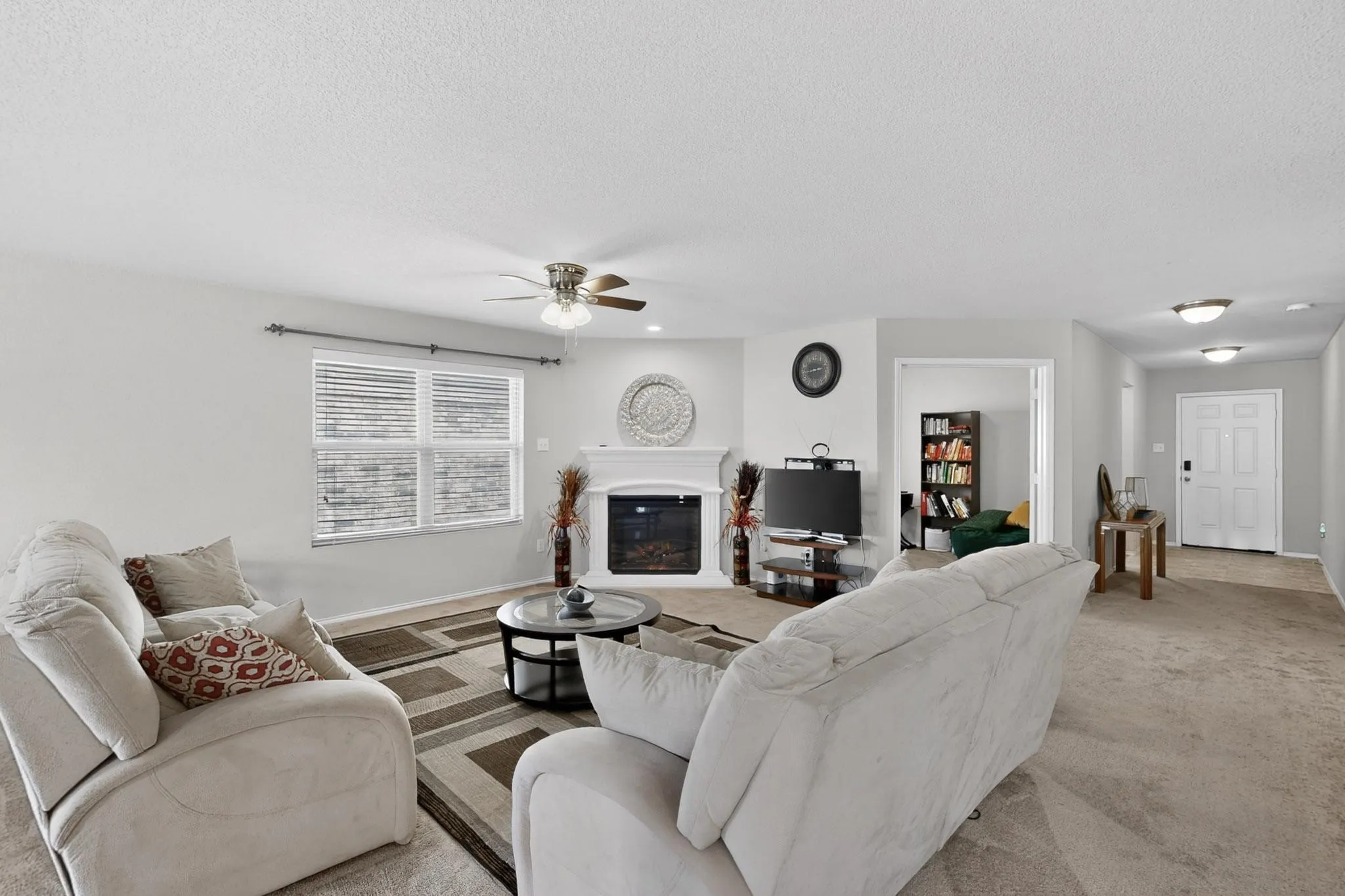 Carpeted living area featuring a glass covered fireplace, a ceiling fan, and a textured ceiling