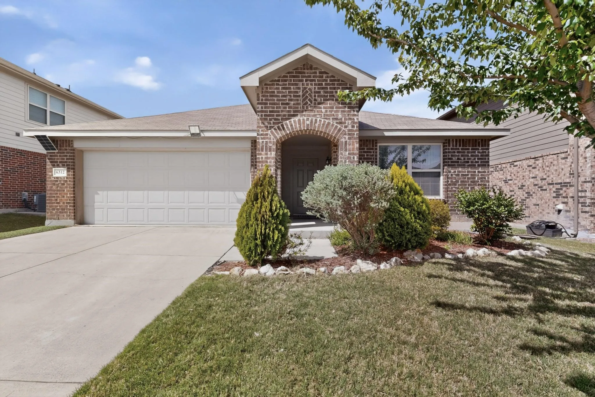 View of front facade with brick siding, an attached garage, driveway, a shingled roof, and a front yard