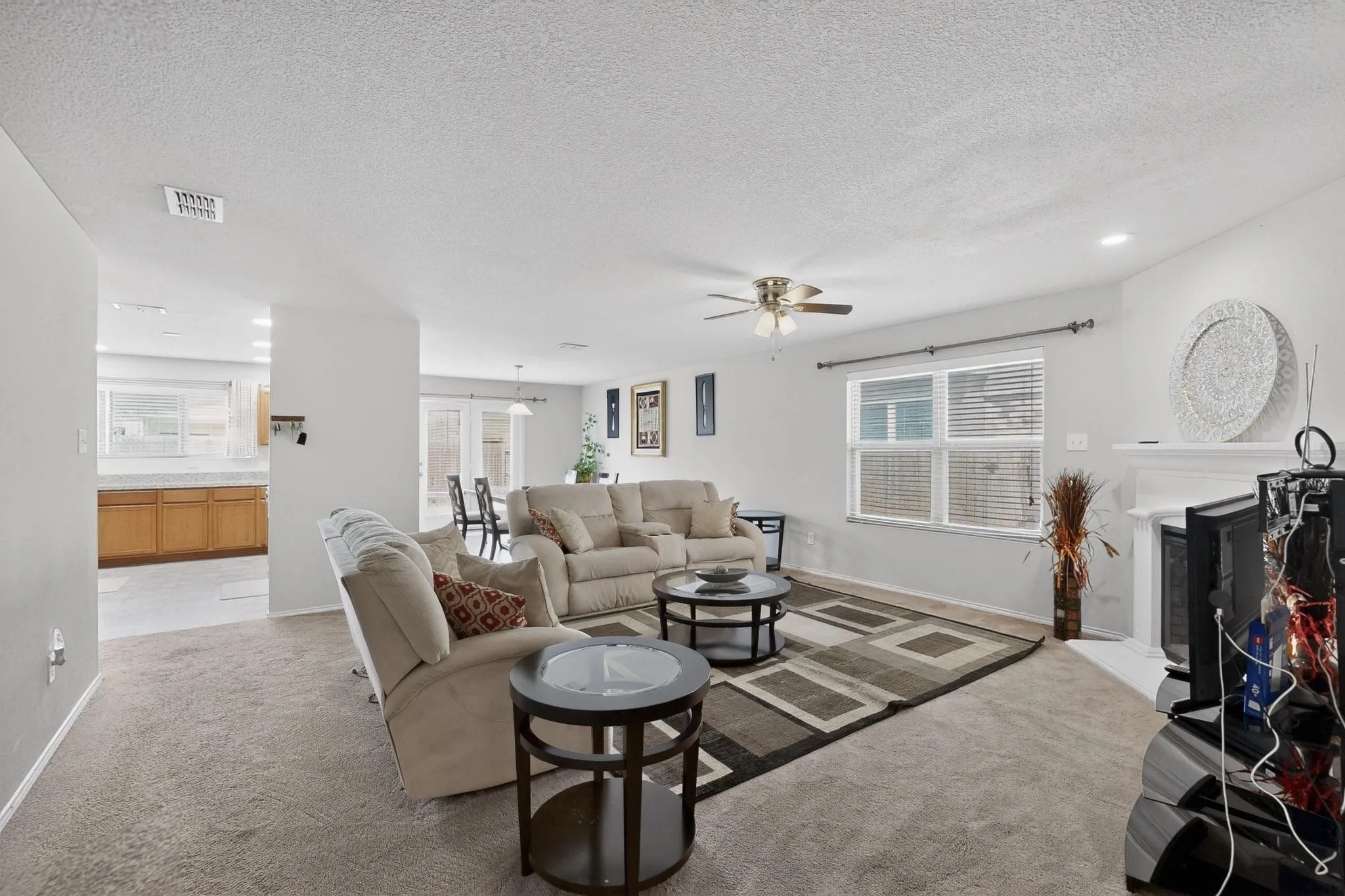 Carpeted living room with a textured ceiling, a fireplace with raised hearth, healthy amount of natural light, a ceiling fan, and recessed lighting
