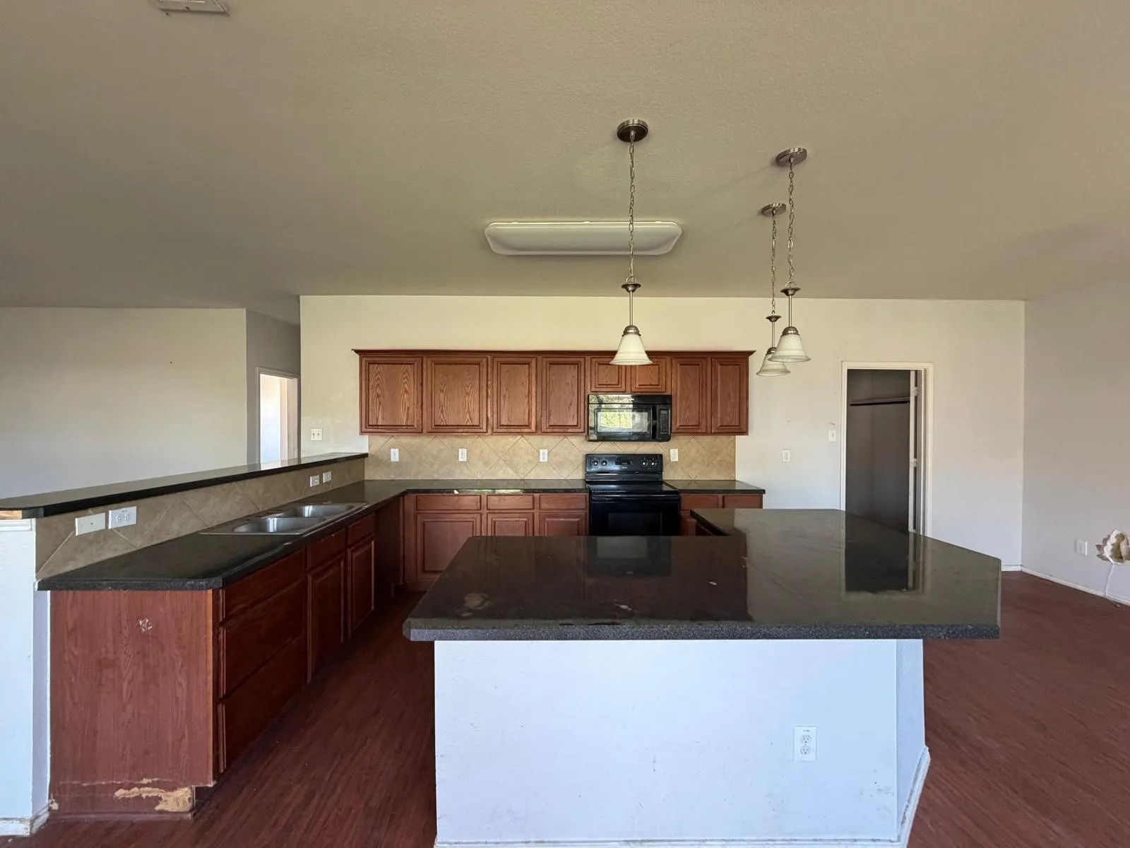 Kitchen featuring black appliances, dark wood-style flooring, a center island, and decorative light fixtures
