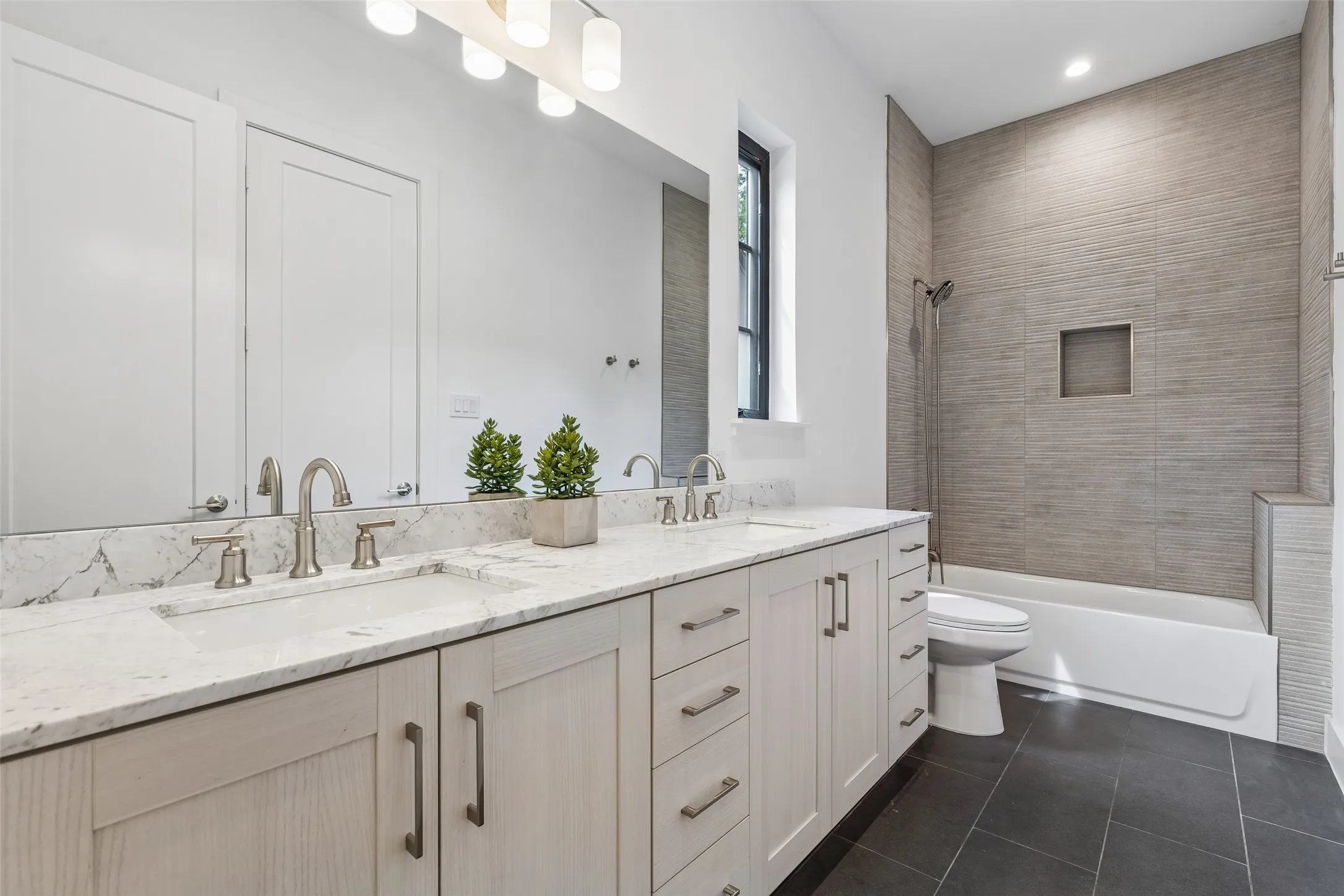Bathroom featuring double vanity, tub / shower combination, and dark tile patterned floors