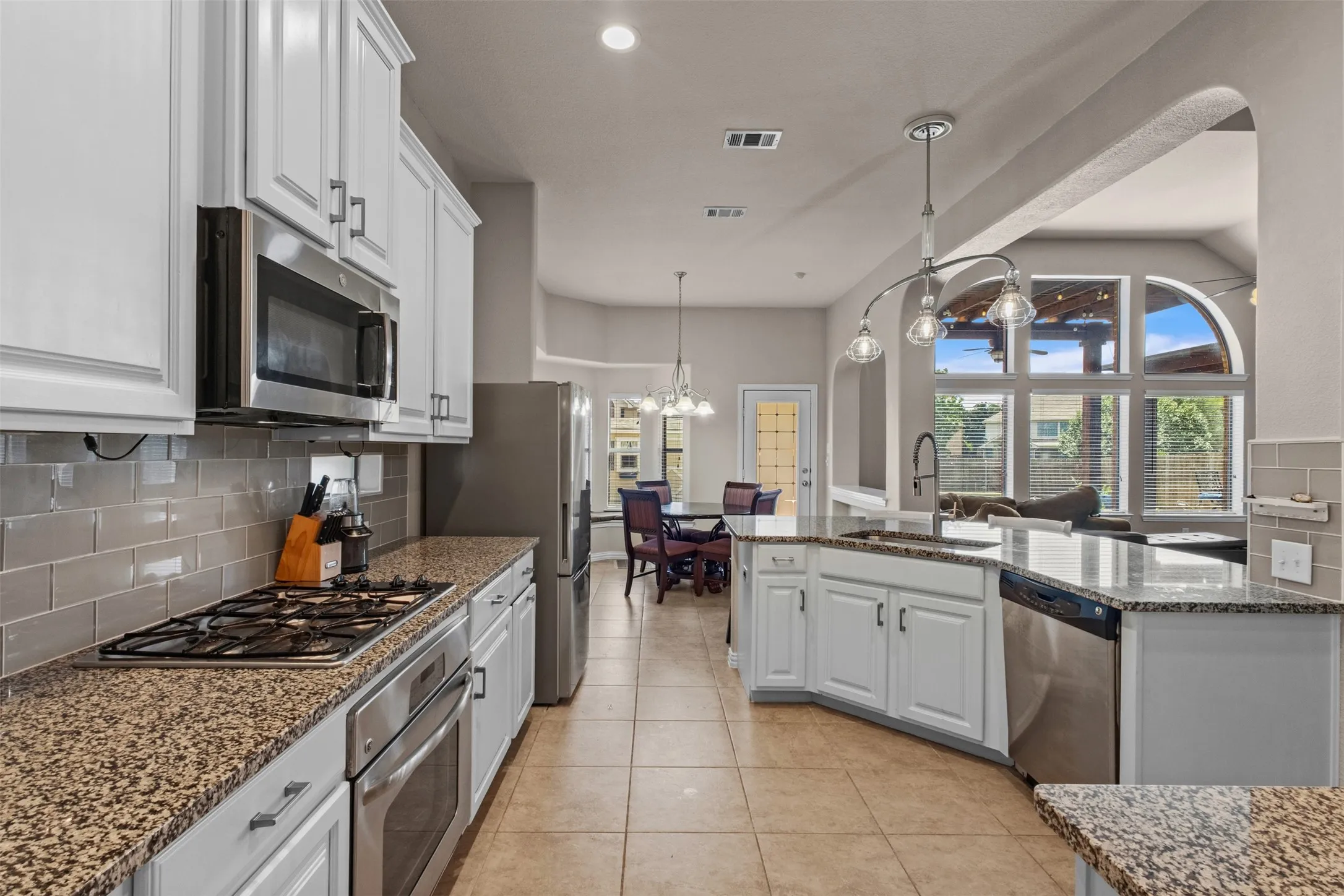 Bright kitchen featuring white cabinetry, granite countertops, stainless steel appliances, a tile backsplash, and tile flooring