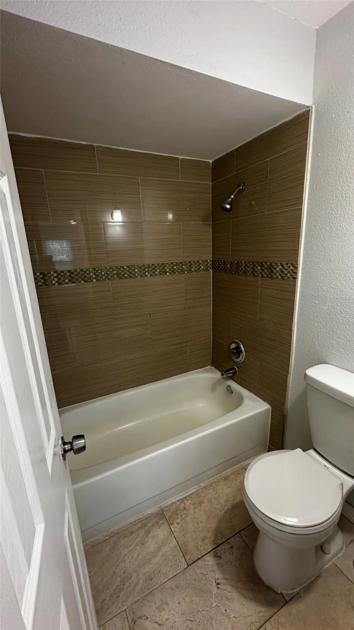Bathroom featuring a white bathtub, ceramic tile flooring, and a shower with brown wall tiles and a decorative mosaic accent band