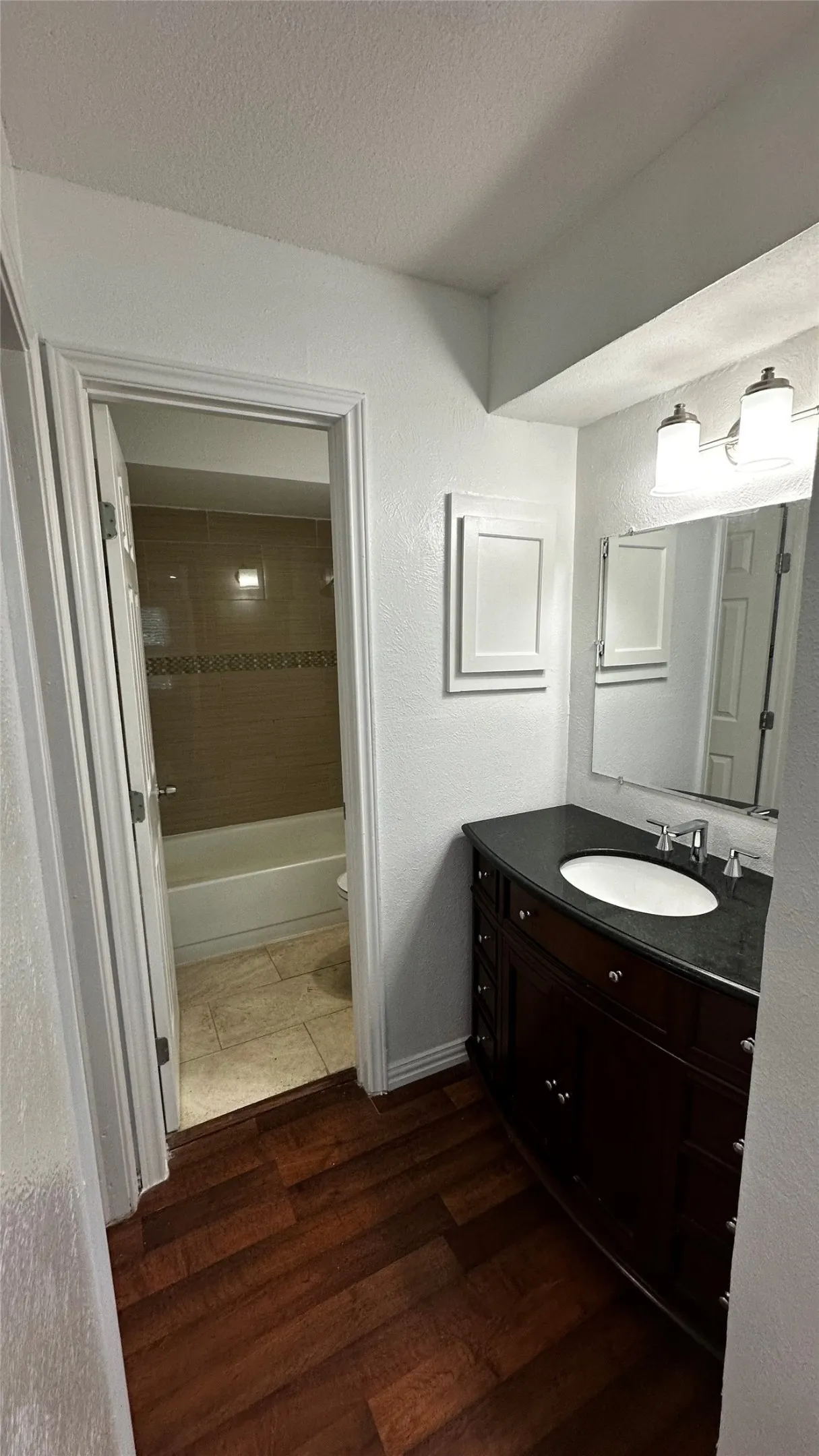 Bathroom featuring wood-finish flooring, a dark wood vanity with a stone countertop, an oval undermount sink, and a two-light fixture