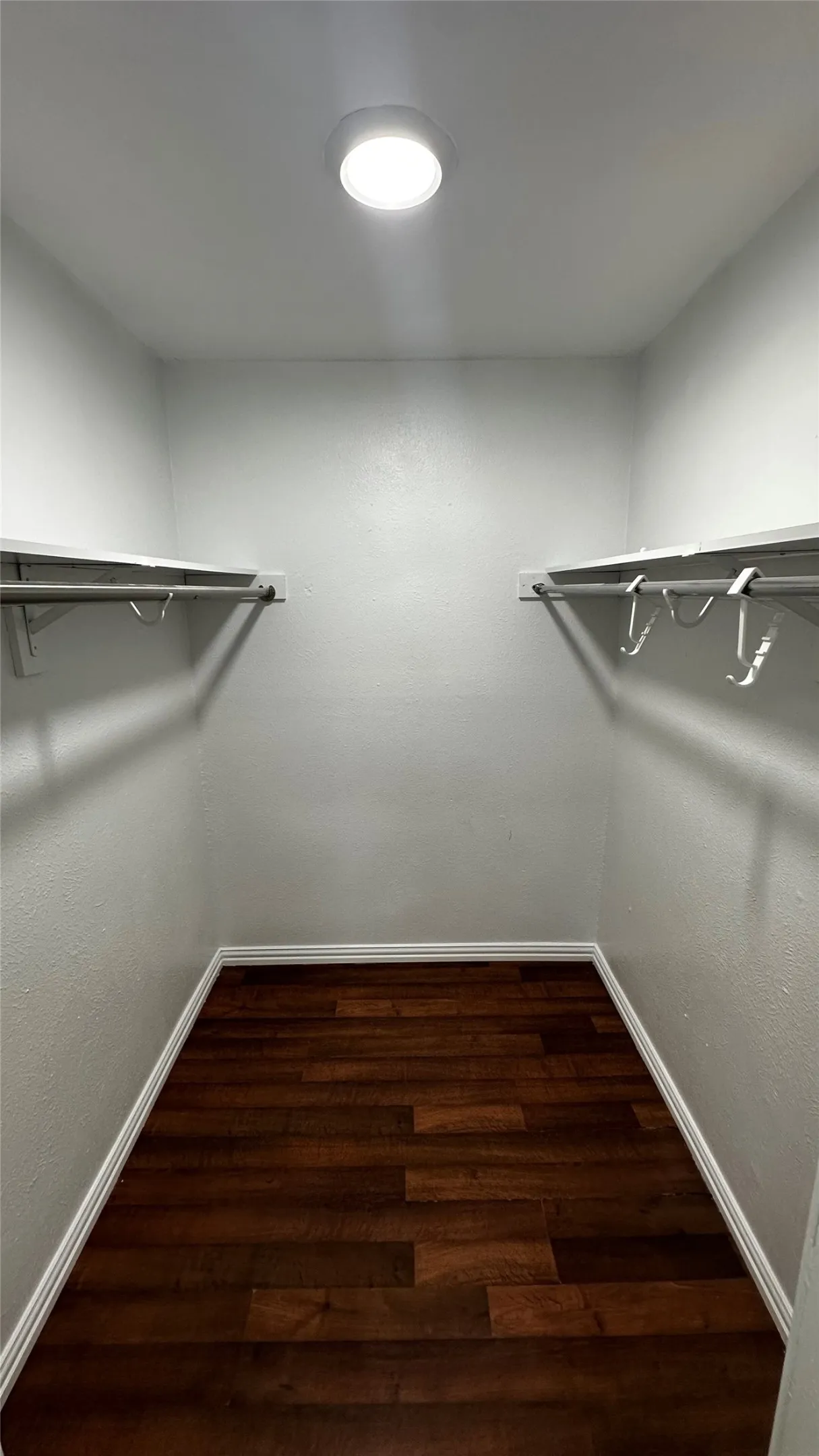 Walk-in closet featuring wood-finish flooring, white walls, recessed ceiling lighting, and dual-level hanging rods