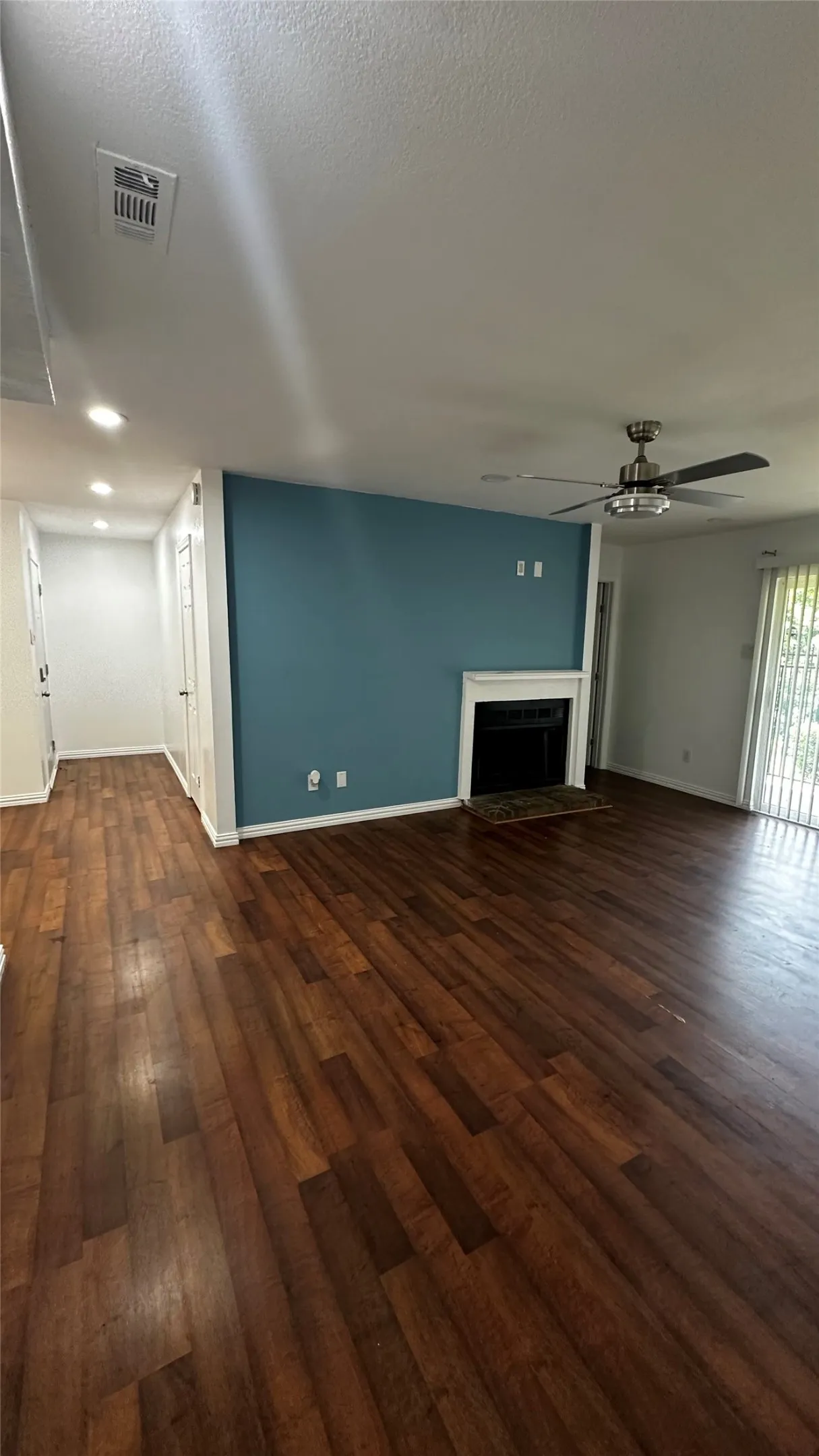 Living area featuring wood-finish flooring, a decorative fireplace with a white mantel, and a ceiling fan