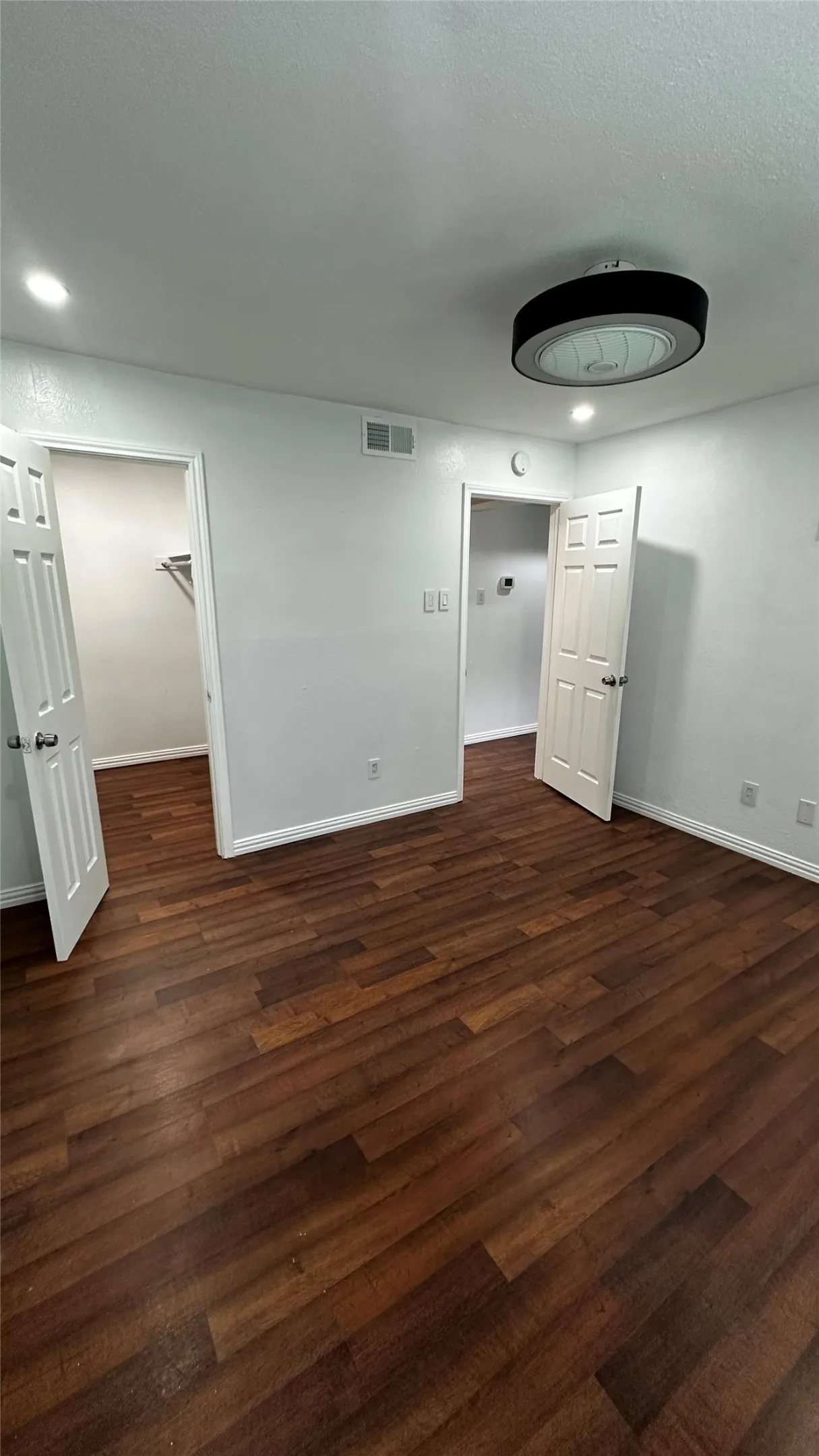 Spacious room featuring dark wood-finish flooring, white baseboards, and light-colored walls