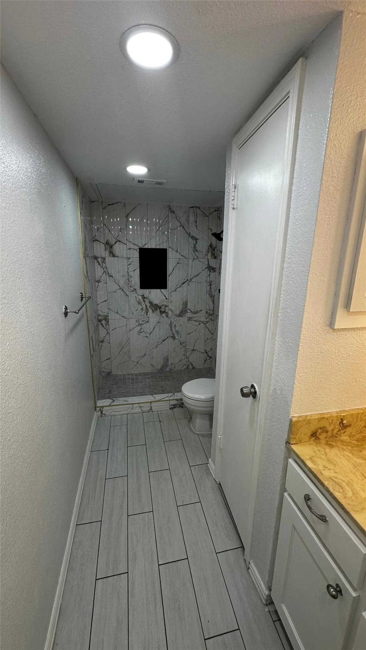 Bathroom with wood-finish tile flooring, recessed lighting, and a walk-in shower featuring marble-look tile walls and a built-in niche