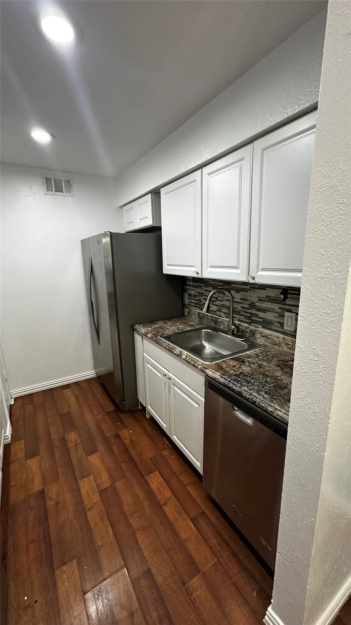 Galley kitchen featuring wood-finish flooring, white cabinetry, a stainless steel sink, and a multi-tone tile backsplash