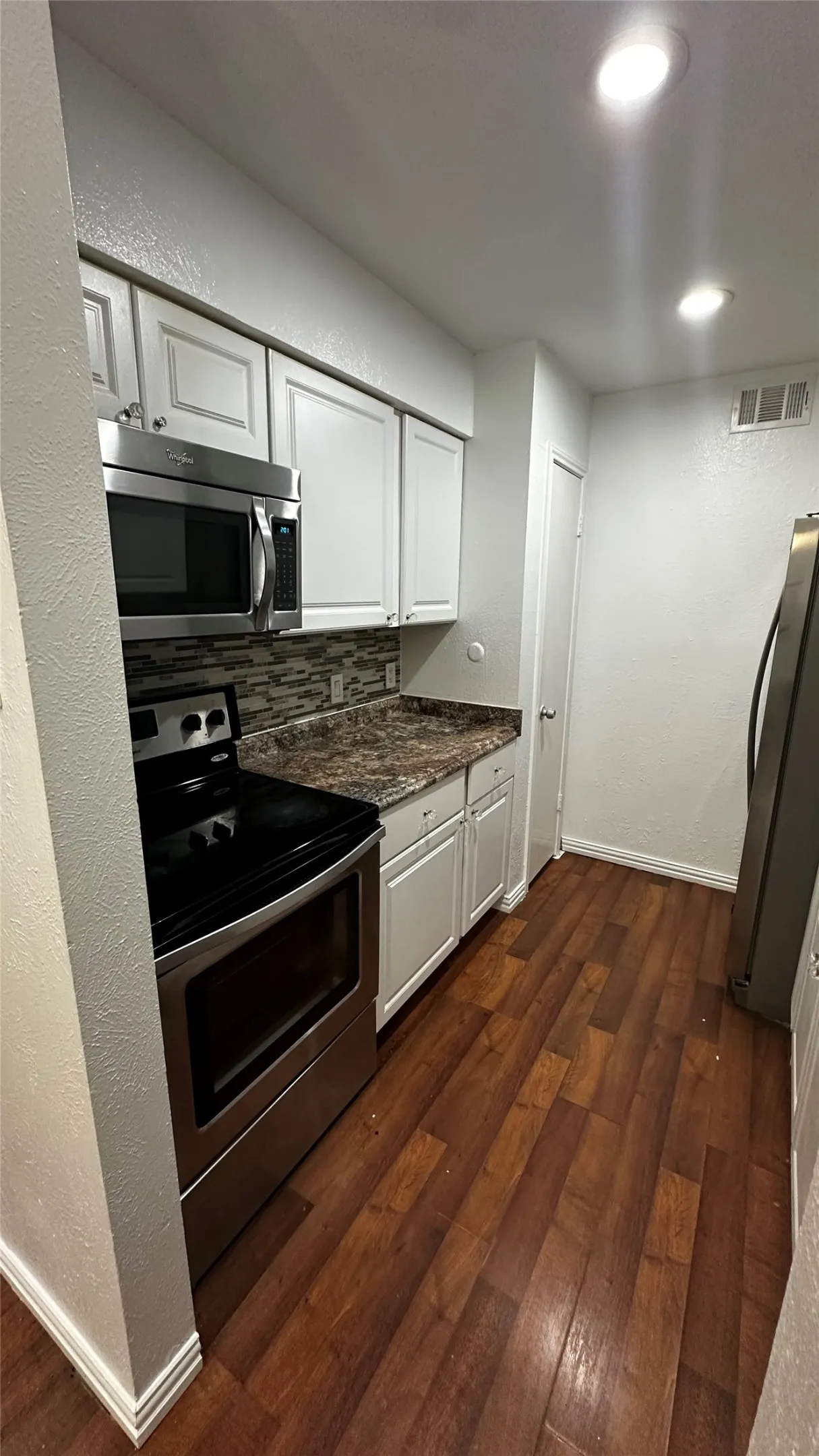 Contemporary kitchen featuring white cabinetry, stainless steel appliances, a mosaic tile backsplash, and wood-finish flooring