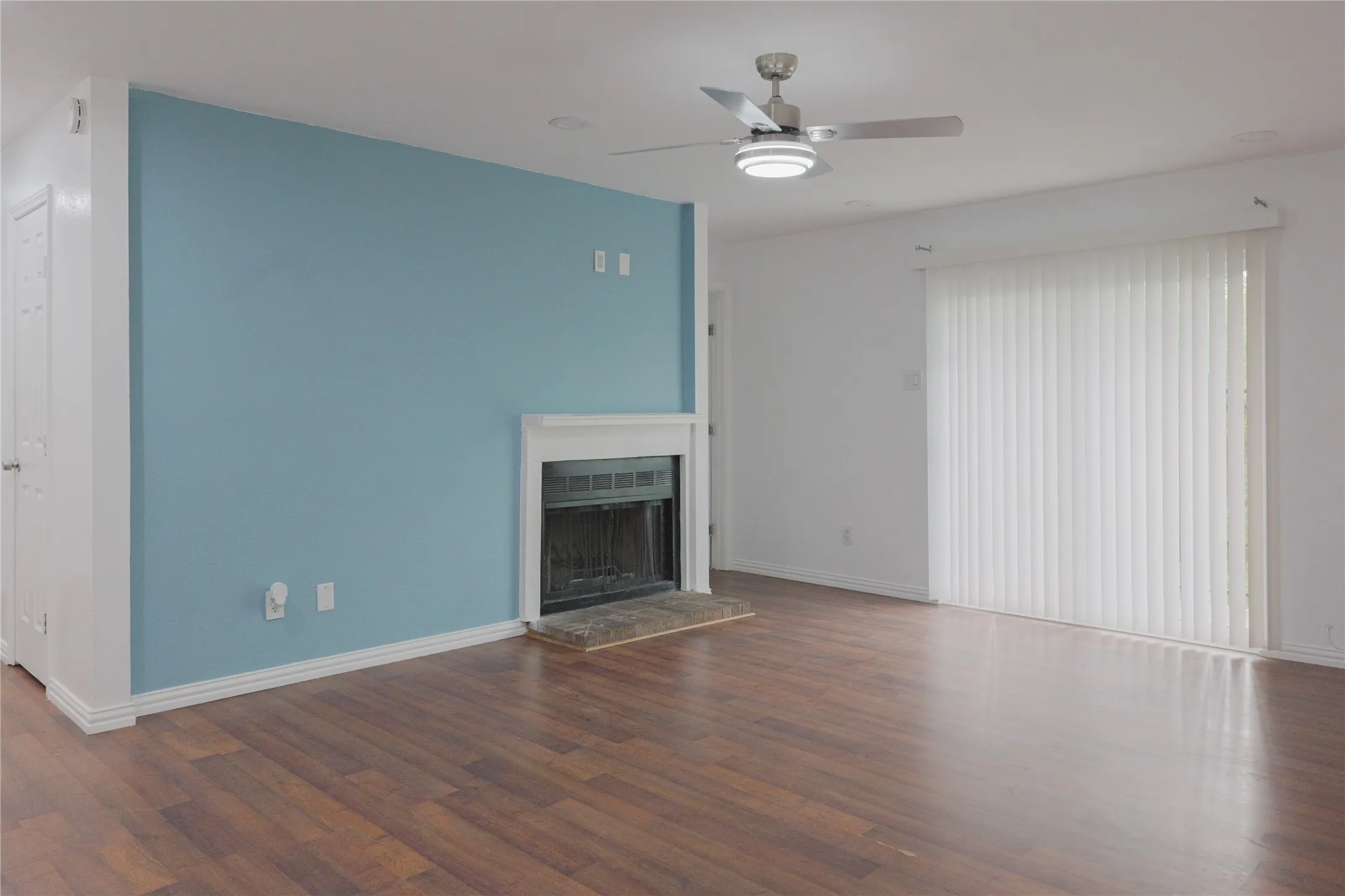 Unfurnished living room with ceiling fan, dark wood-style floors, and a fireplace with raised hearth