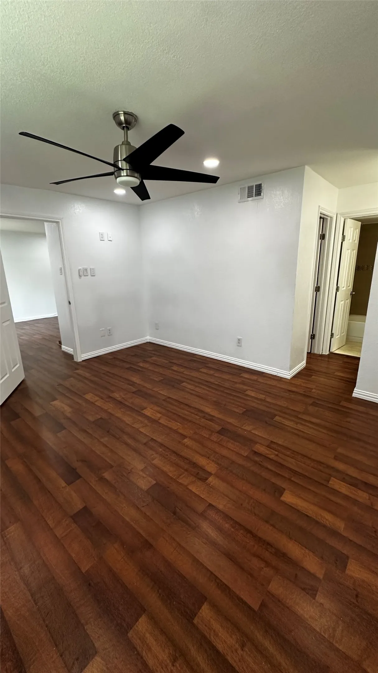 Spacious room featuring rich wood-finish flooring, recessed lighting, and a modern ceiling fan with black blades and a brushed nickel base