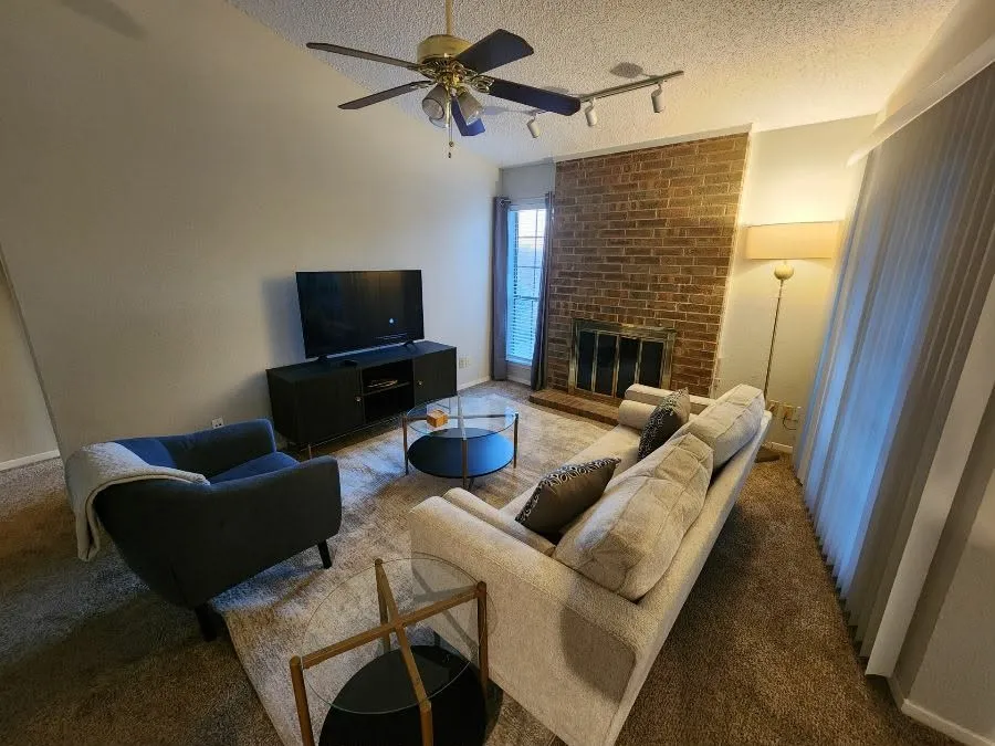 Carpeted living room featuring track lighting, ceiling fan, a textured ceiling, and a brick fireplace