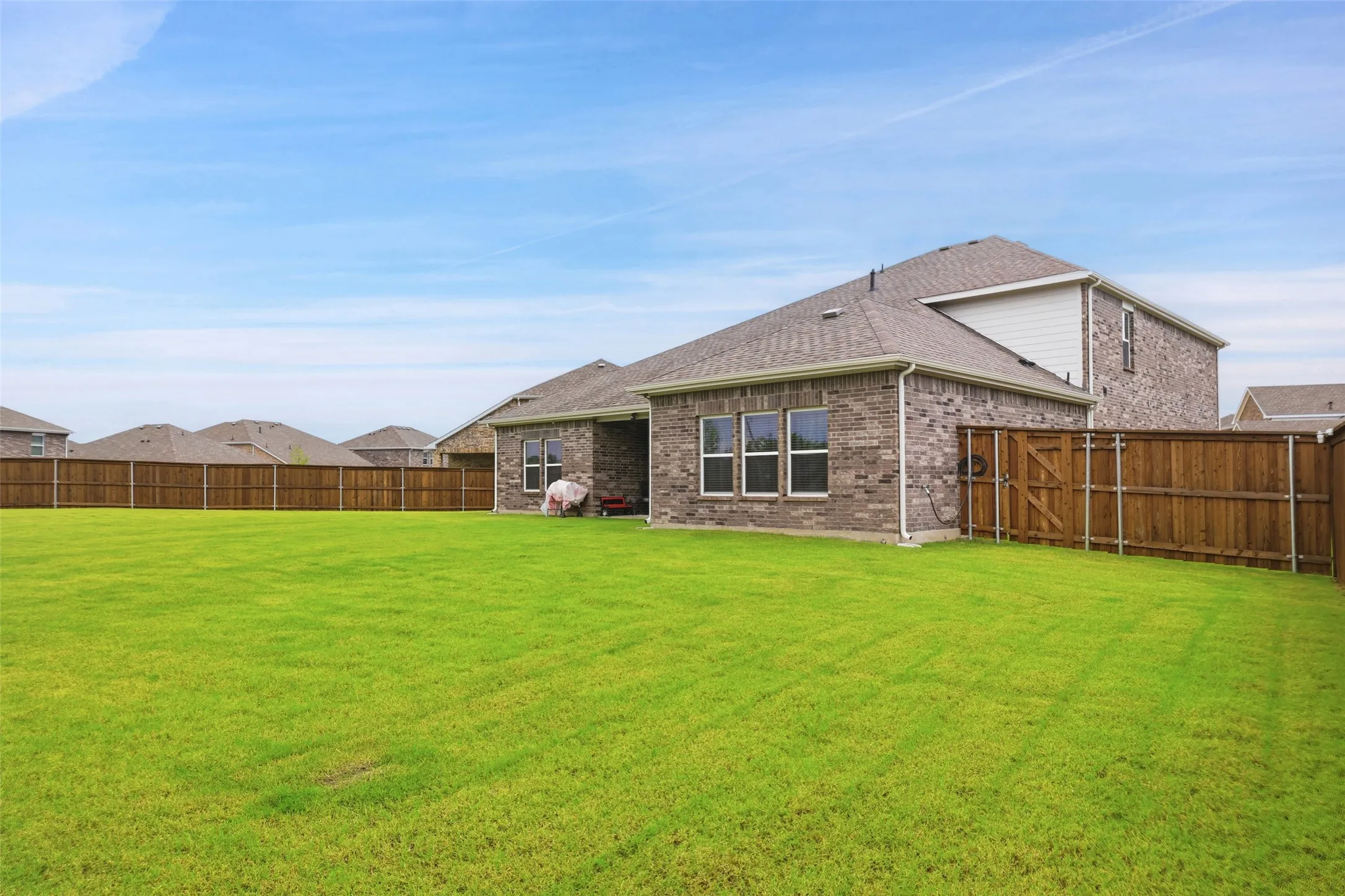 Expansive backyard featuring a lush green lawn, full wood-plank fencing, a two-story brick exterior, and multiple windows providing interior light