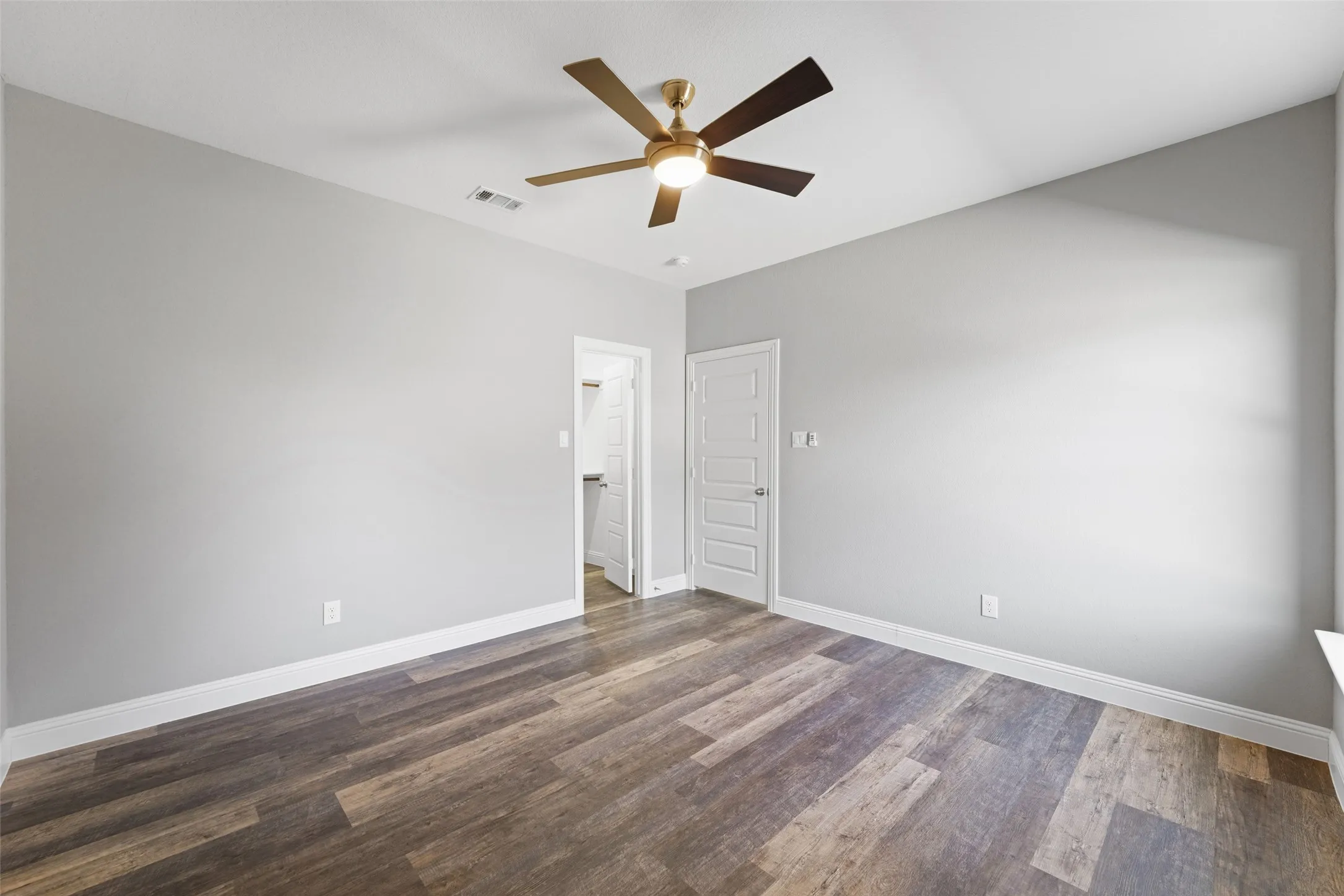 Unfurnished bedroom with dark wood-style floors, ceiling fan, and a walk in closet
