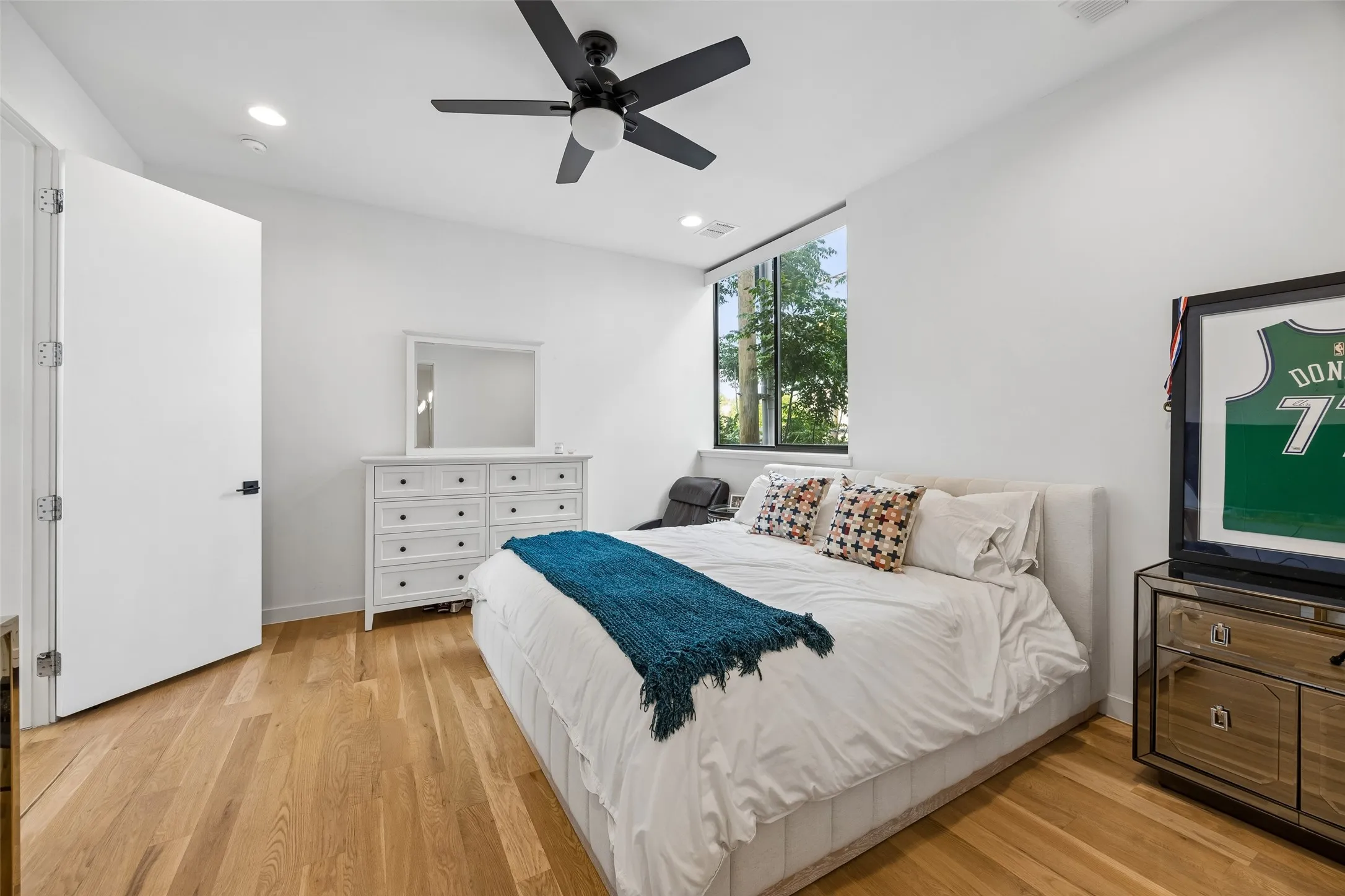This room features hardwood flooring, a ceiling fan with integrated lighting, and white walls