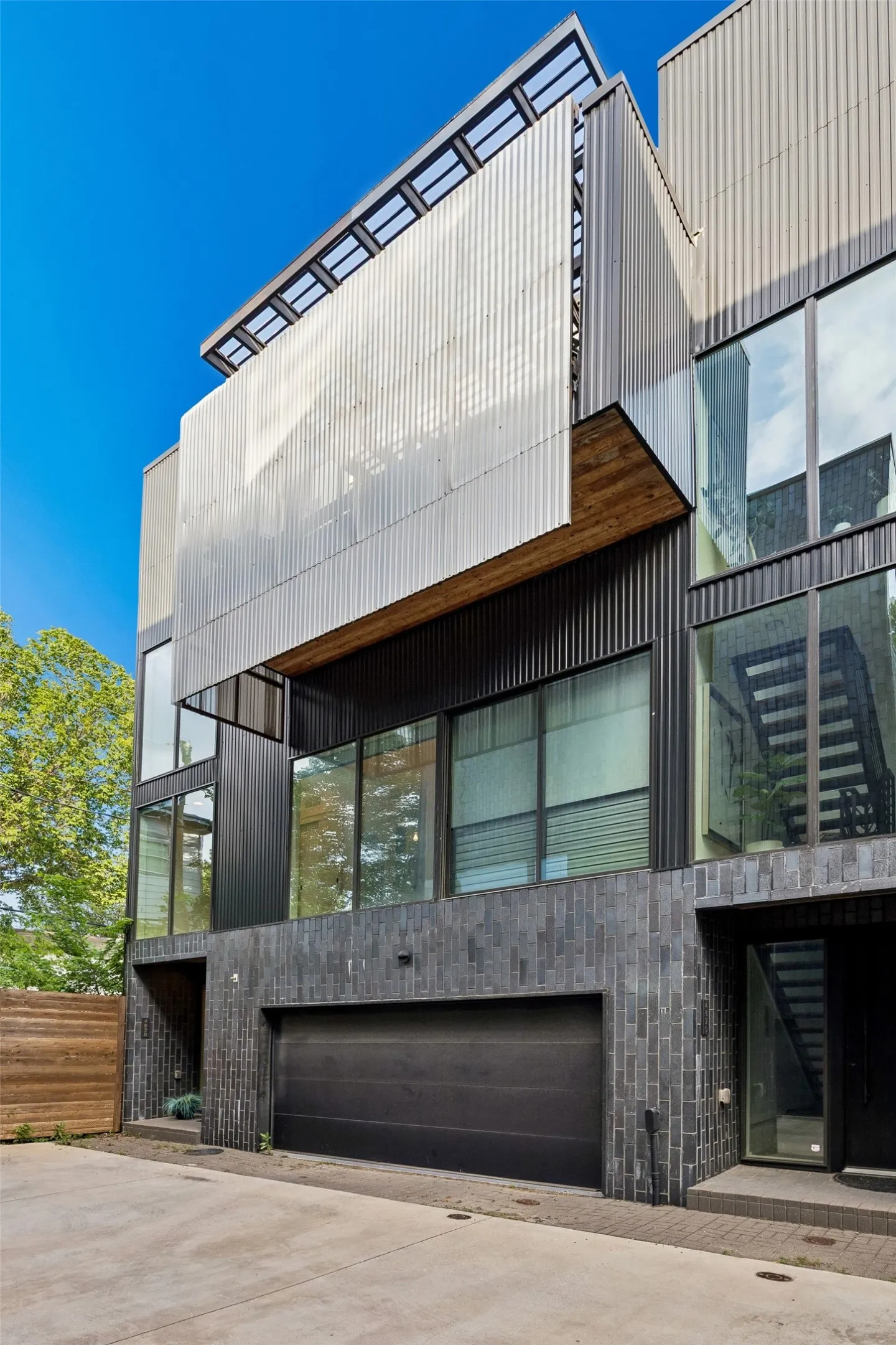 Modern multi-level property with an integrated garage, large windows, and a distinctive corrugated metal façade