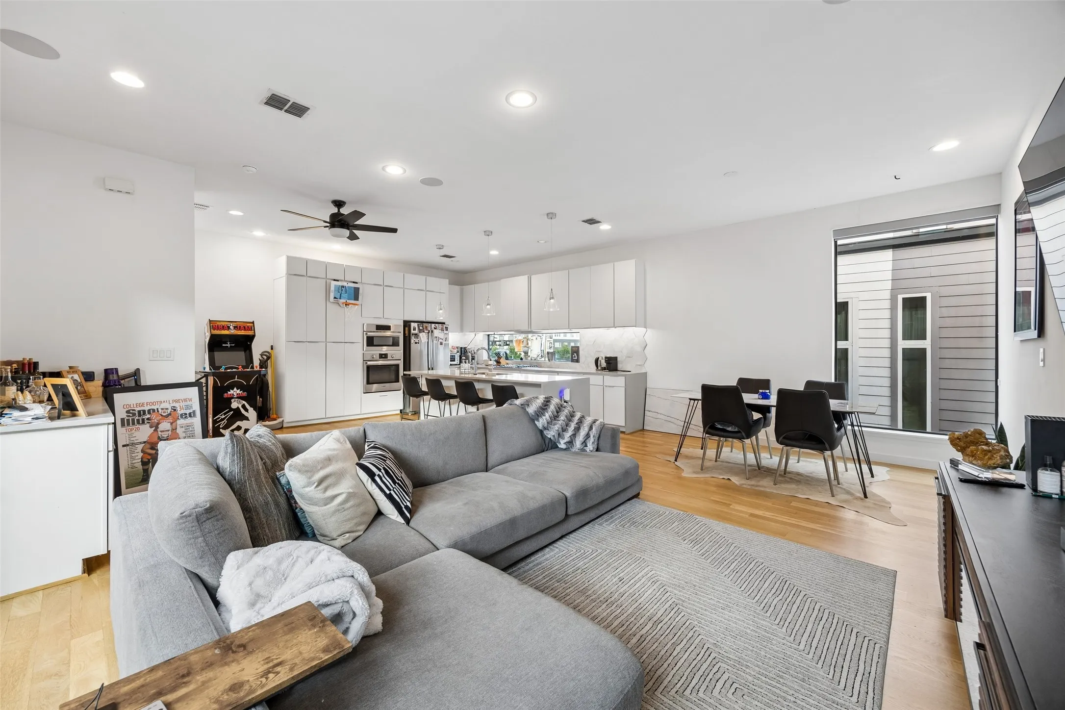 This open-concept living area features hardwood floors, recessed lighting, and a modern ceiling fan