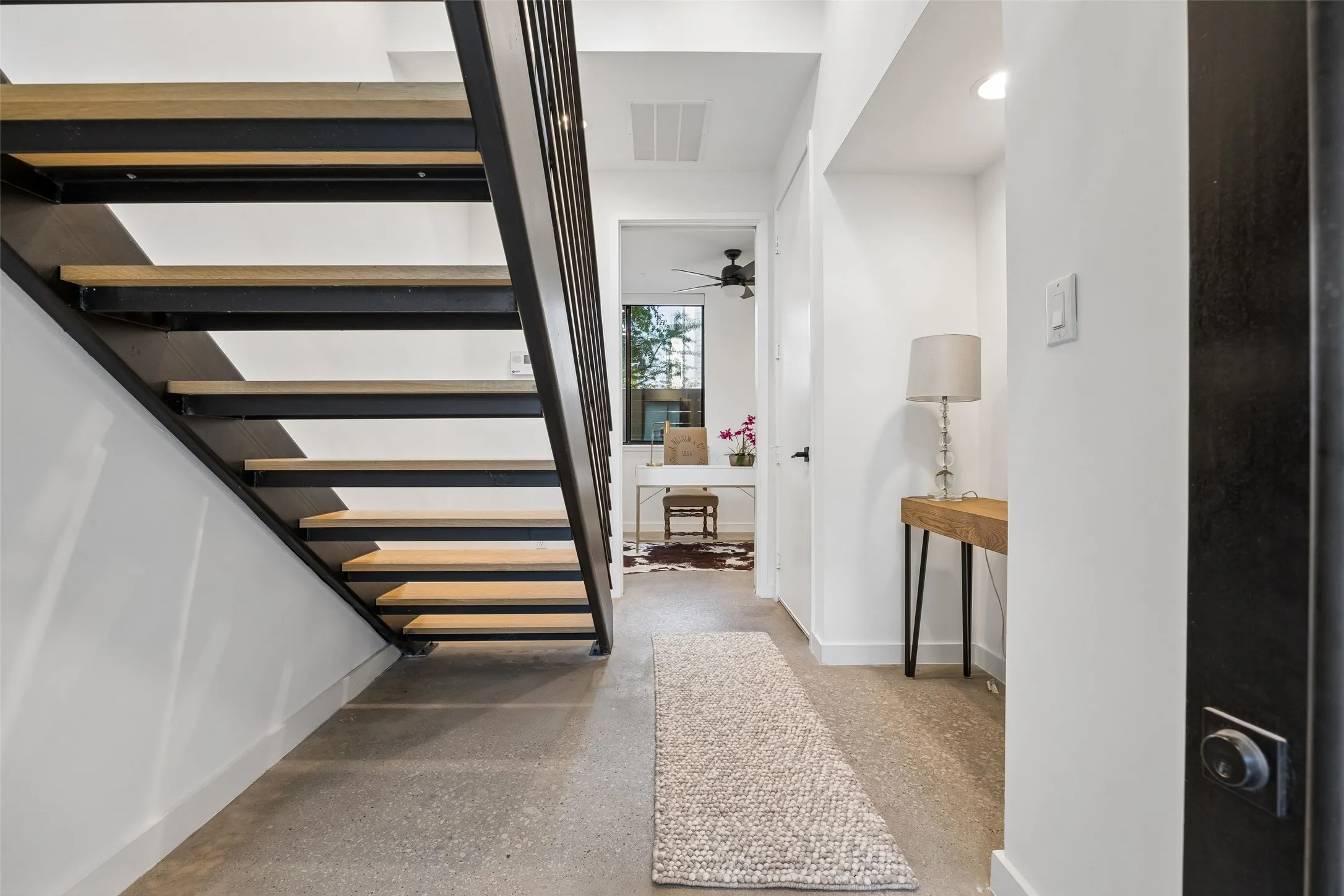 Entryway featuring an open-riser staircase with wood treads and a dark metal railing, concrete flooring, and a console table